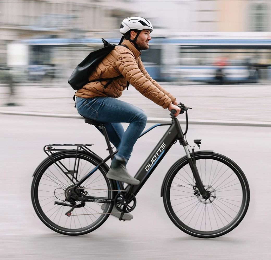 Uomo guida e-bike in città, indossa giacca marrone e casco.