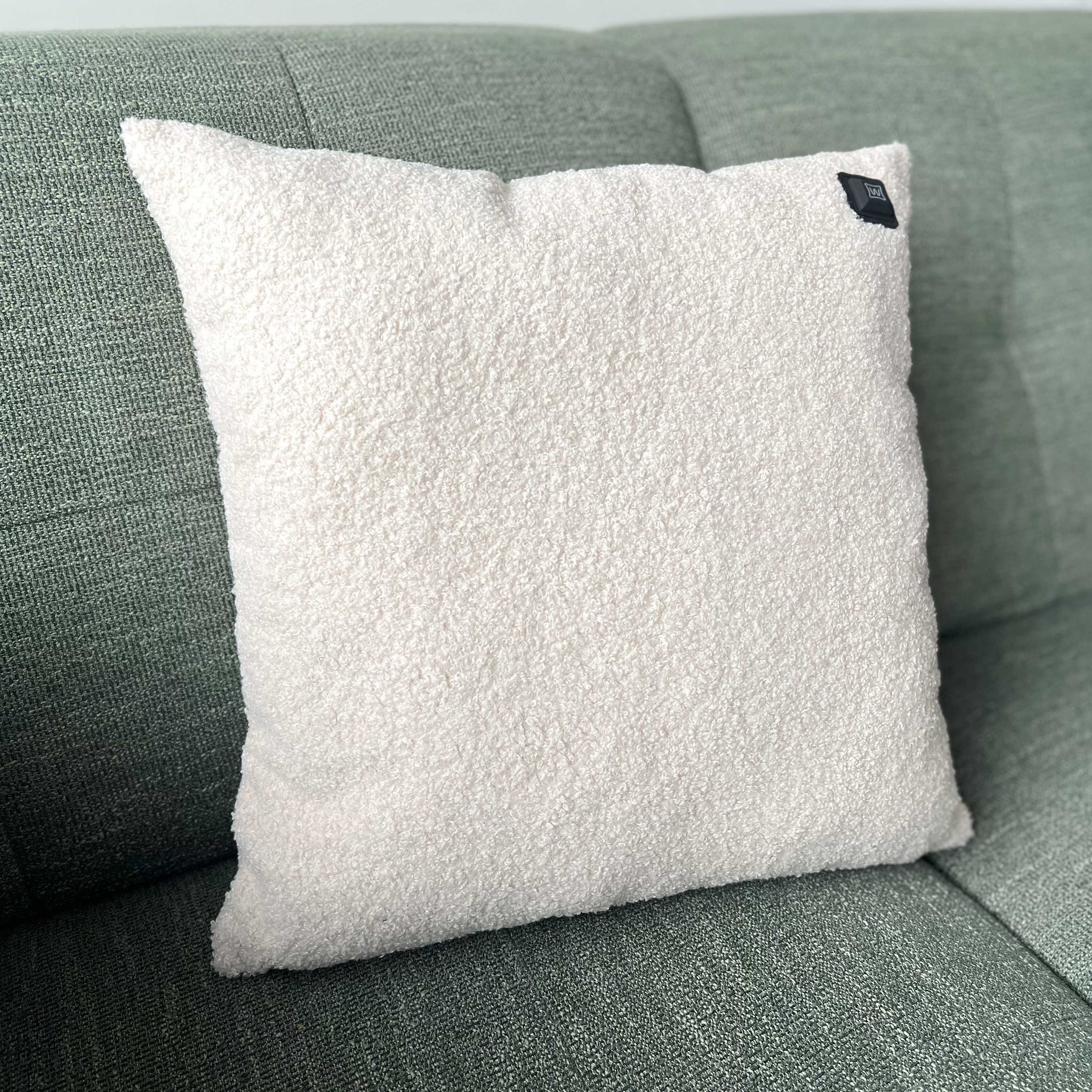 Ein weißes Teddyfell-Kissen liegt auf einem grünen Sofa.