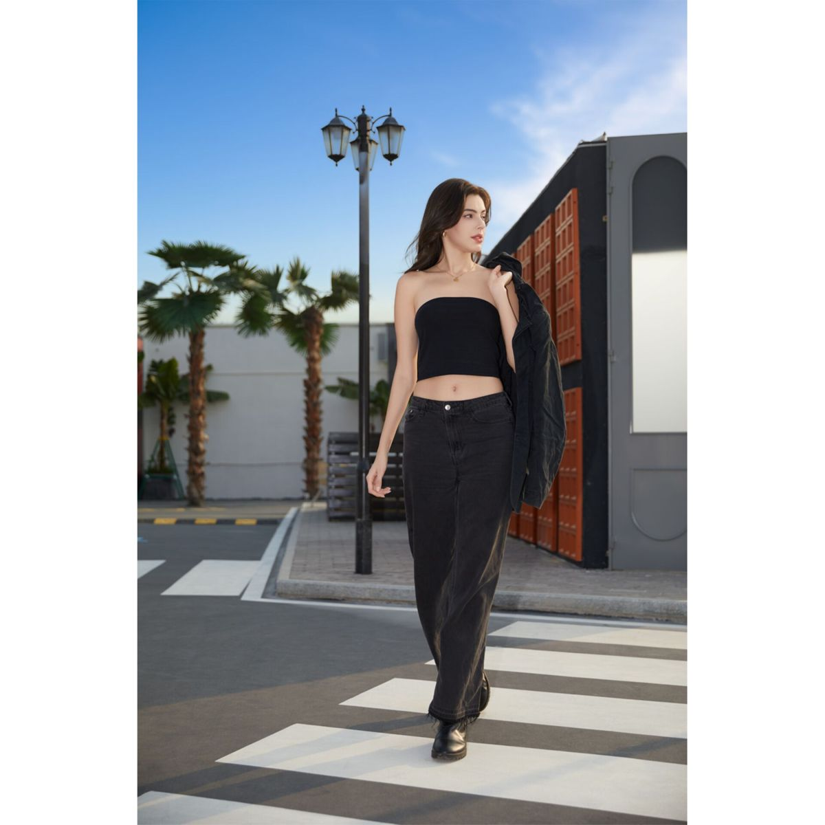 Una donna in crop top nero e jeans attraversa un passaggio pedonale.