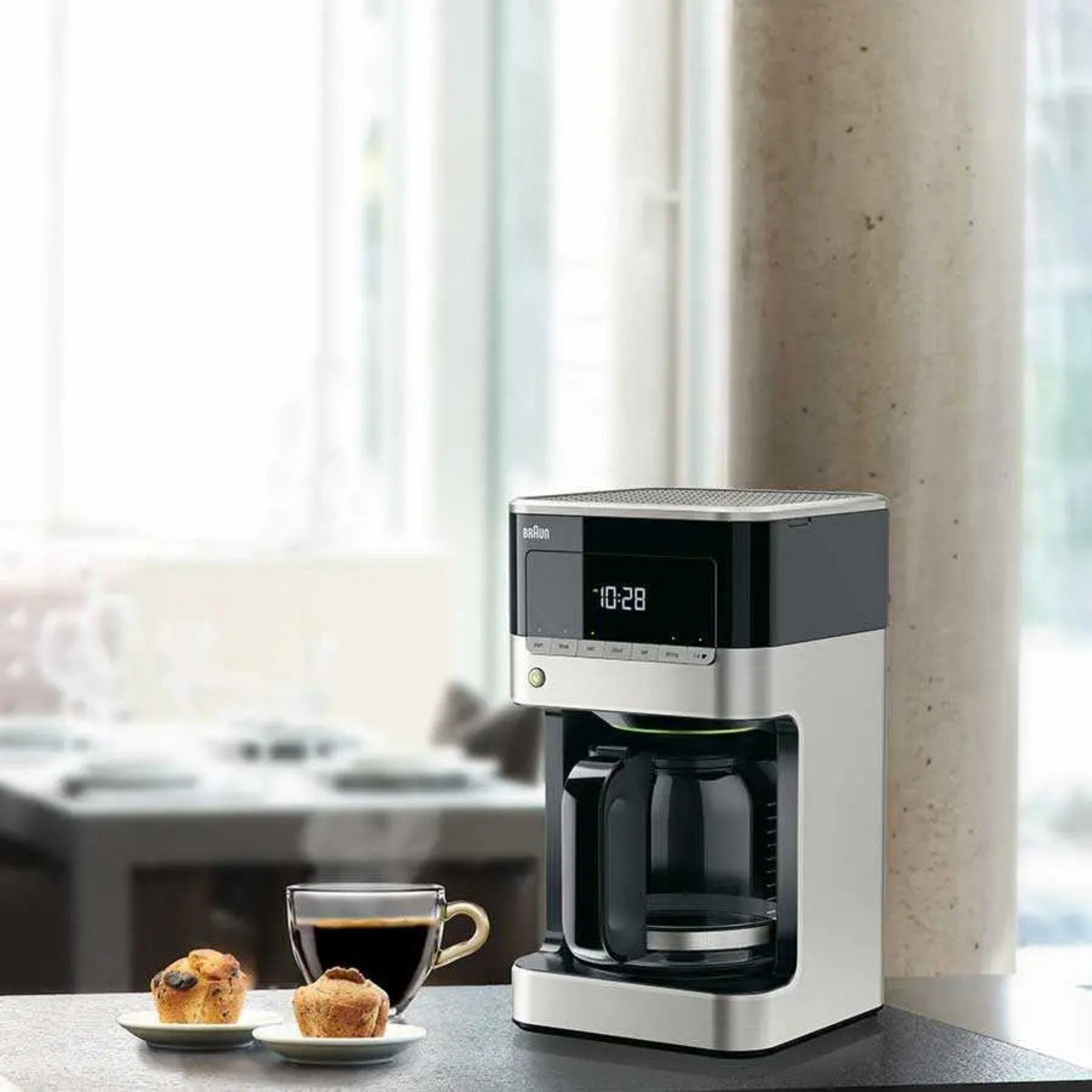 Ekspres do kawy z dzbankiem, filiżanka kawy i dwa muffiny na stole.