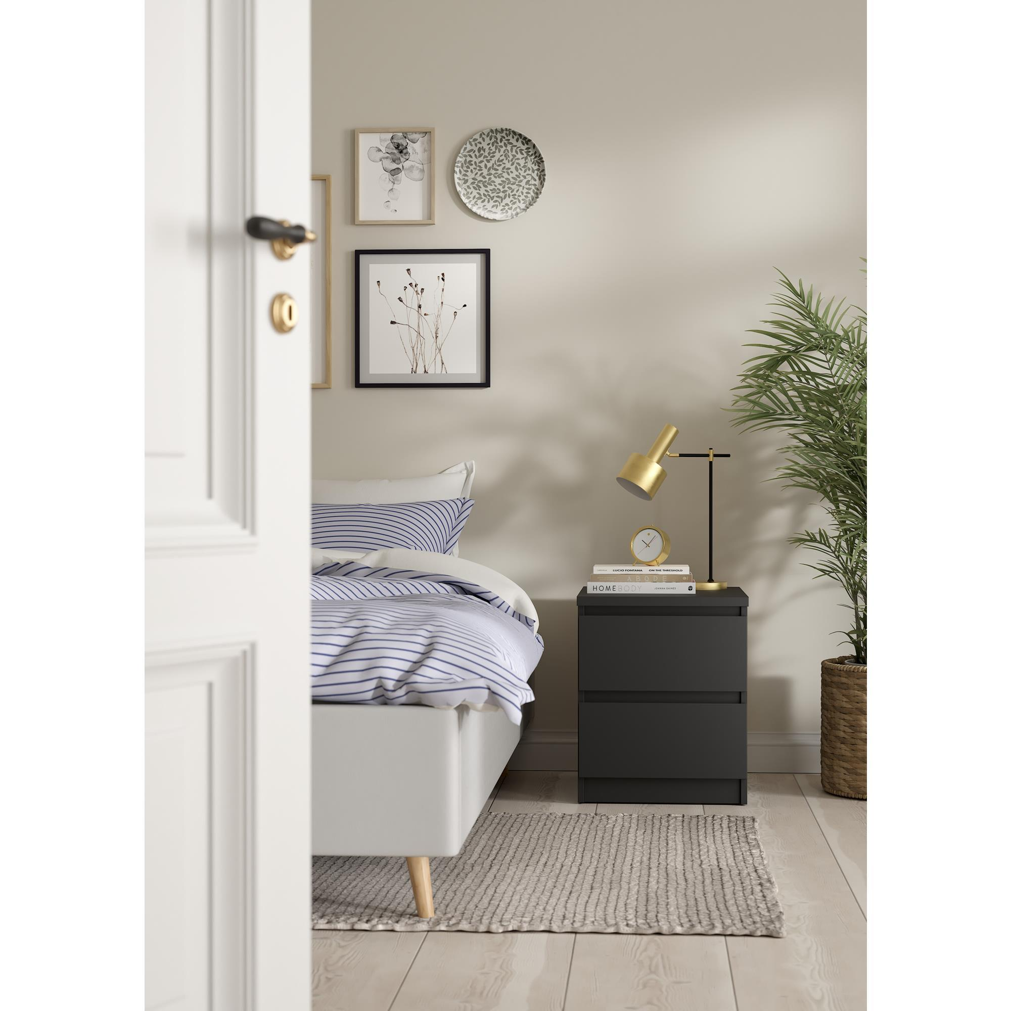 Dormitorio con cama, mesita de noche, lámpara, reloj y plantas.