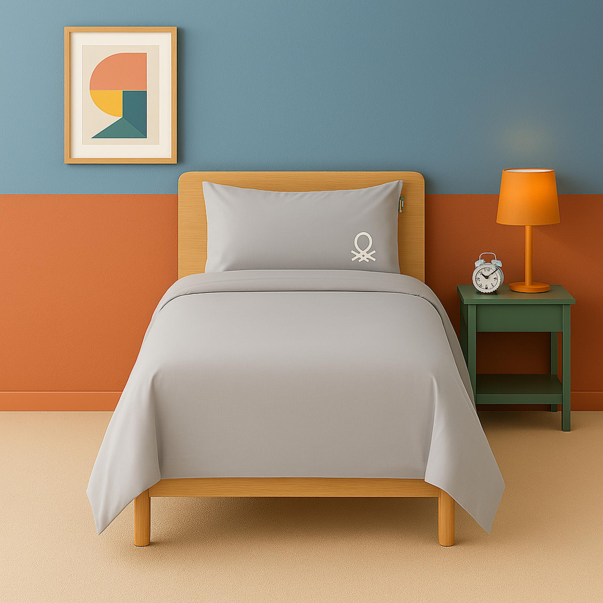 Una cama con ropa de cama gris, una mesita de noche con lámpara y despertador.