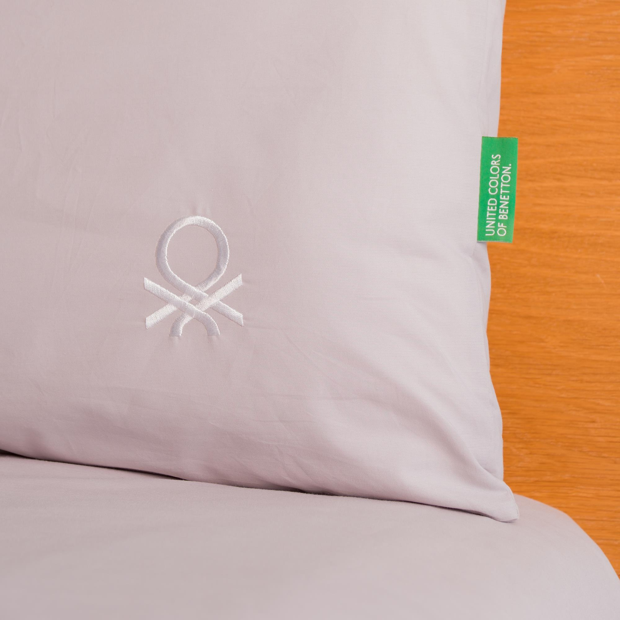 Cojín gris claro con logo blanco y etiqueta verde. Fondo de madera.
