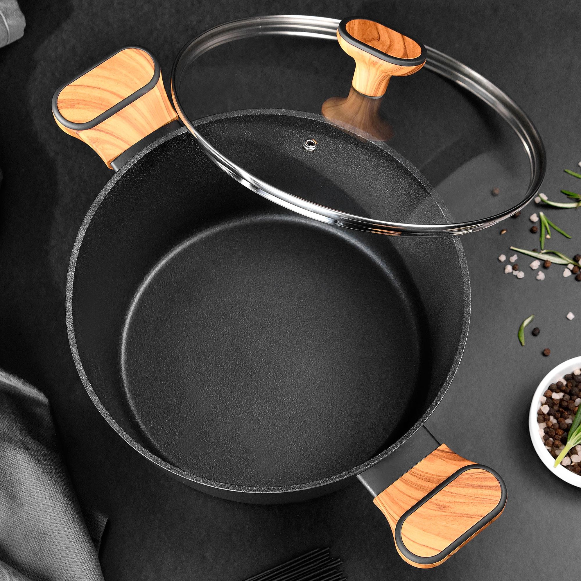 Olla negra con asas de madera y tapa de cristal, especias cerca.