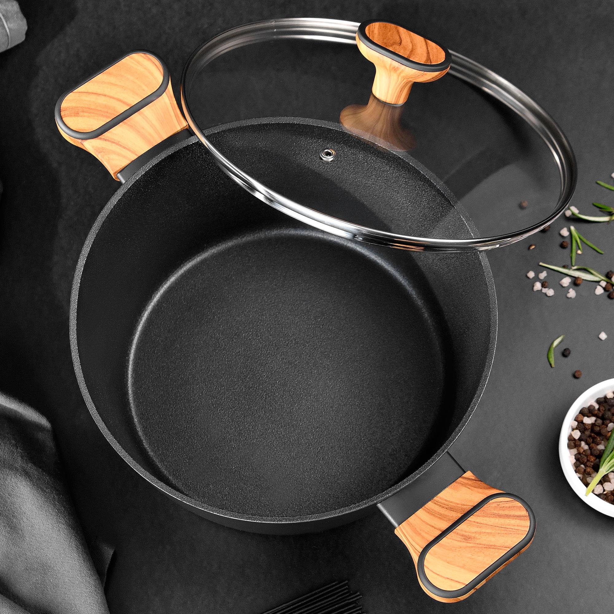 Olla negra con tapa de cristal y asas de madera, junto a especias.