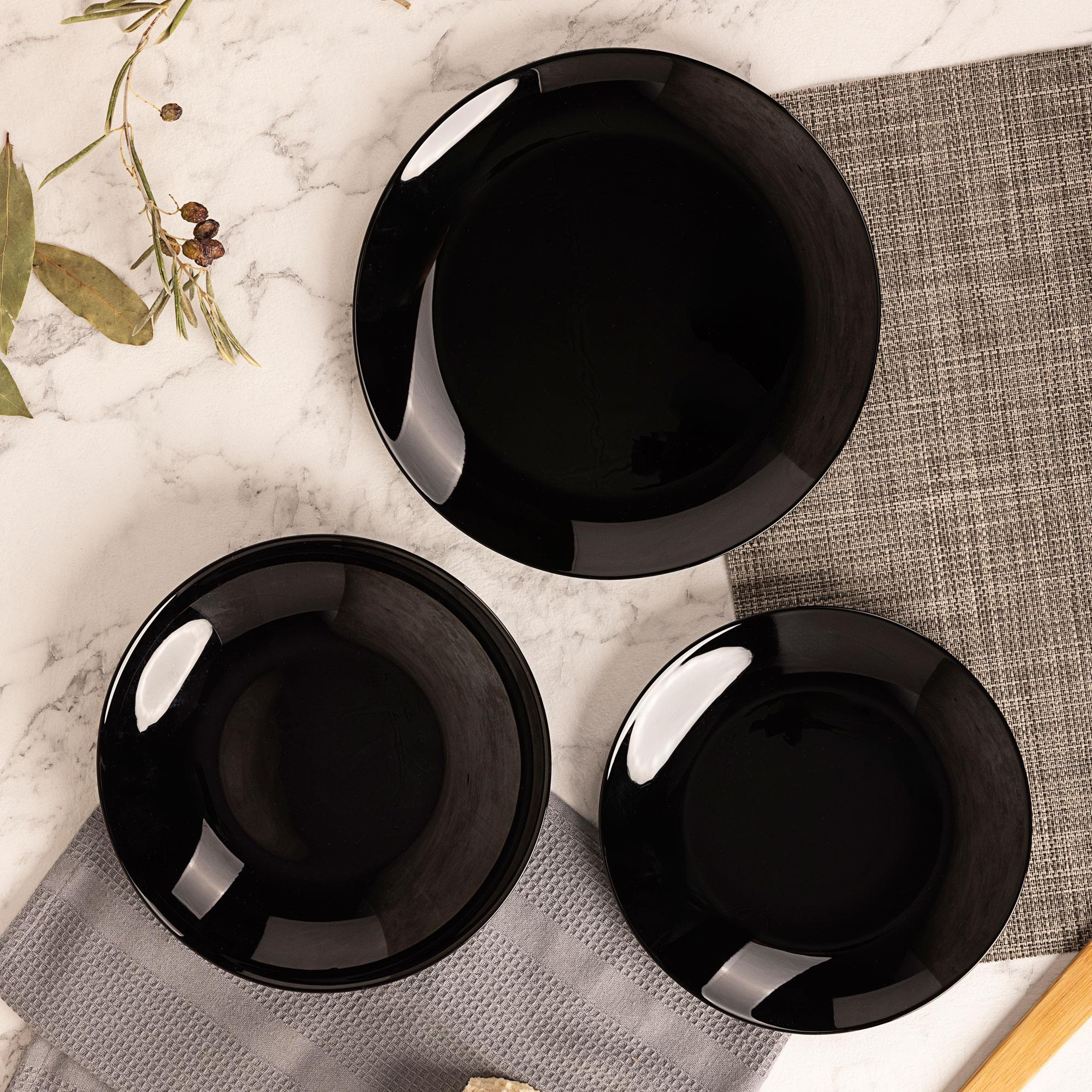 Tres platos negros sobre mármol y un mantel.