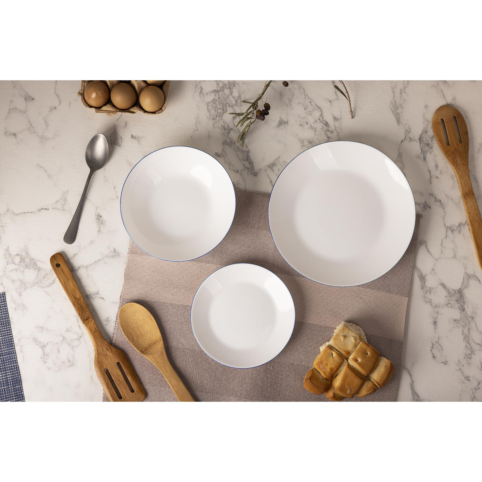 Platos blancos, huevos, pan, cuchara y utensilios de madera en mesa mármol.