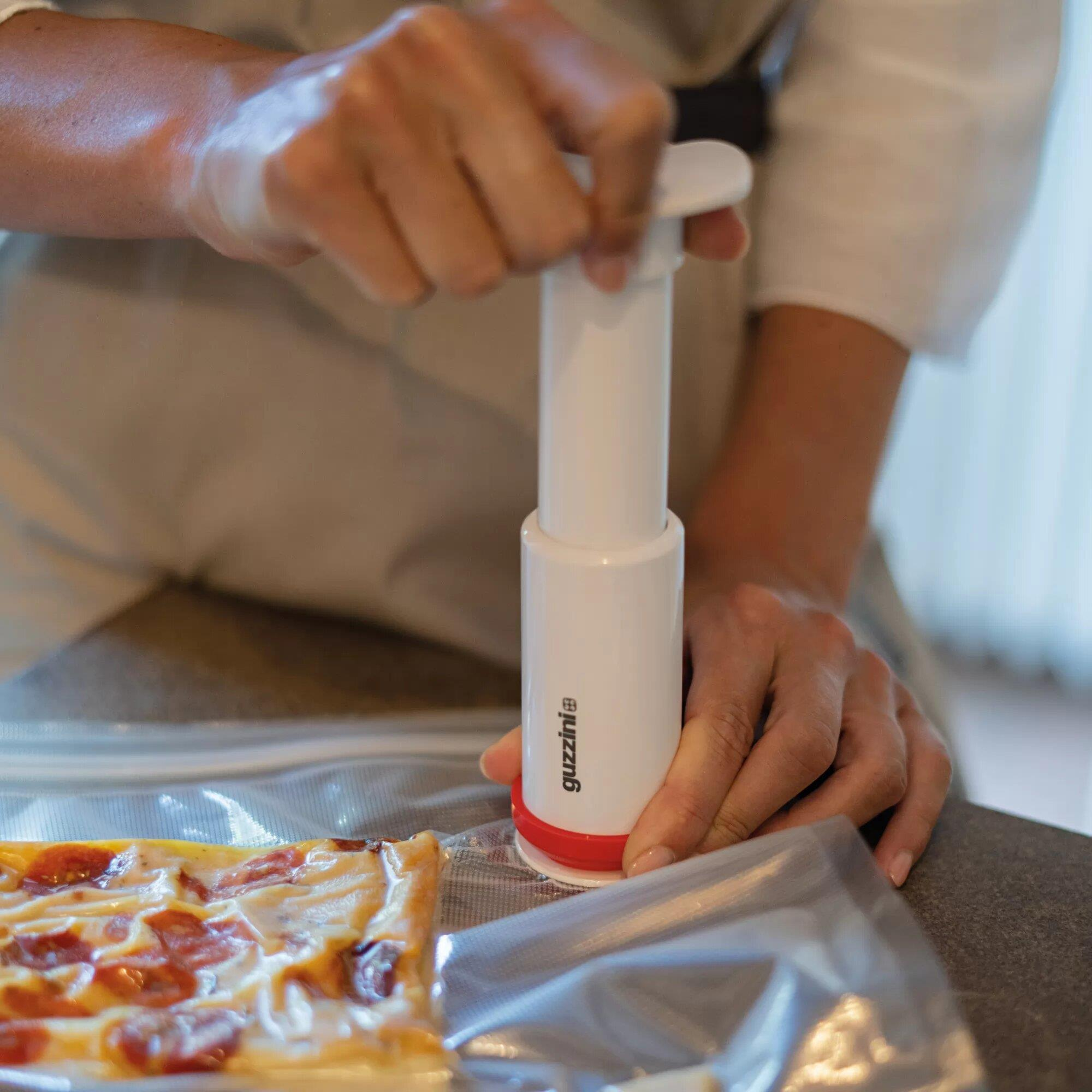 Una mano usa una bomba blanca para sacar aire de una bolsa de vacío con pizza.