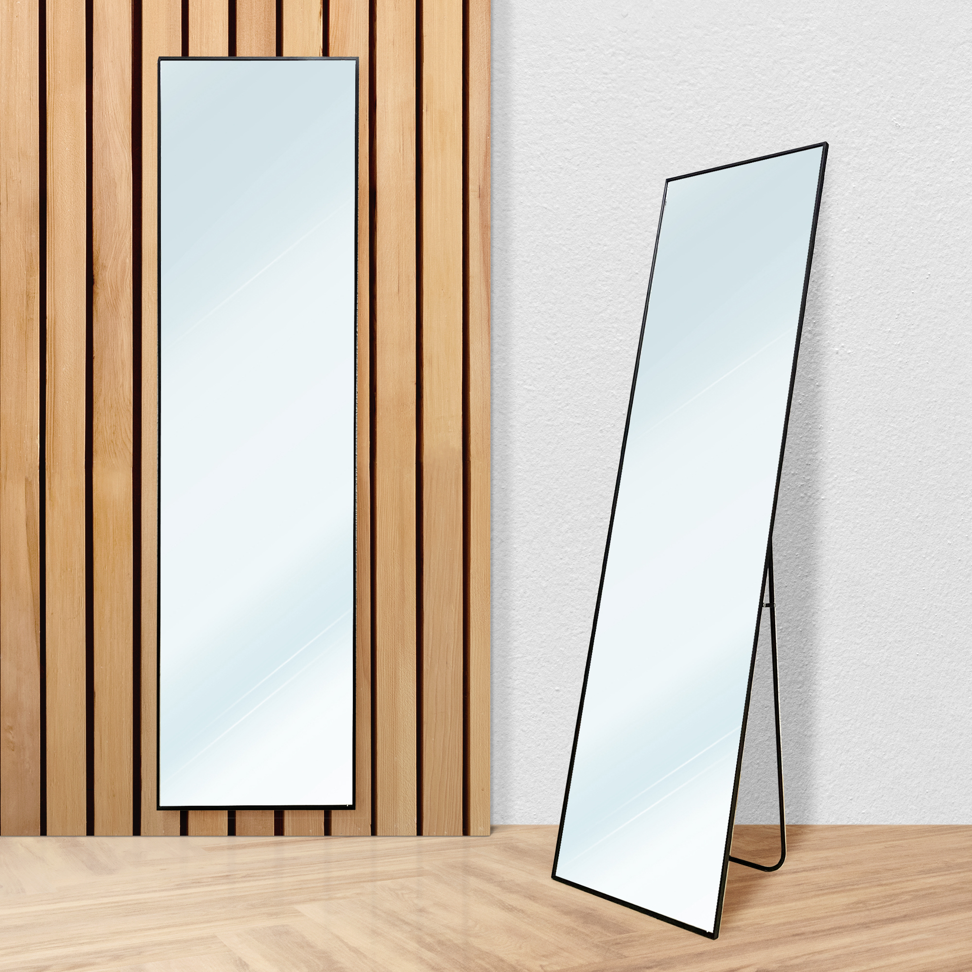 Dos espejos esbeltos se alzan uno al lado del otro sobre suelo de madera, contra panel de madera y pared blanca.