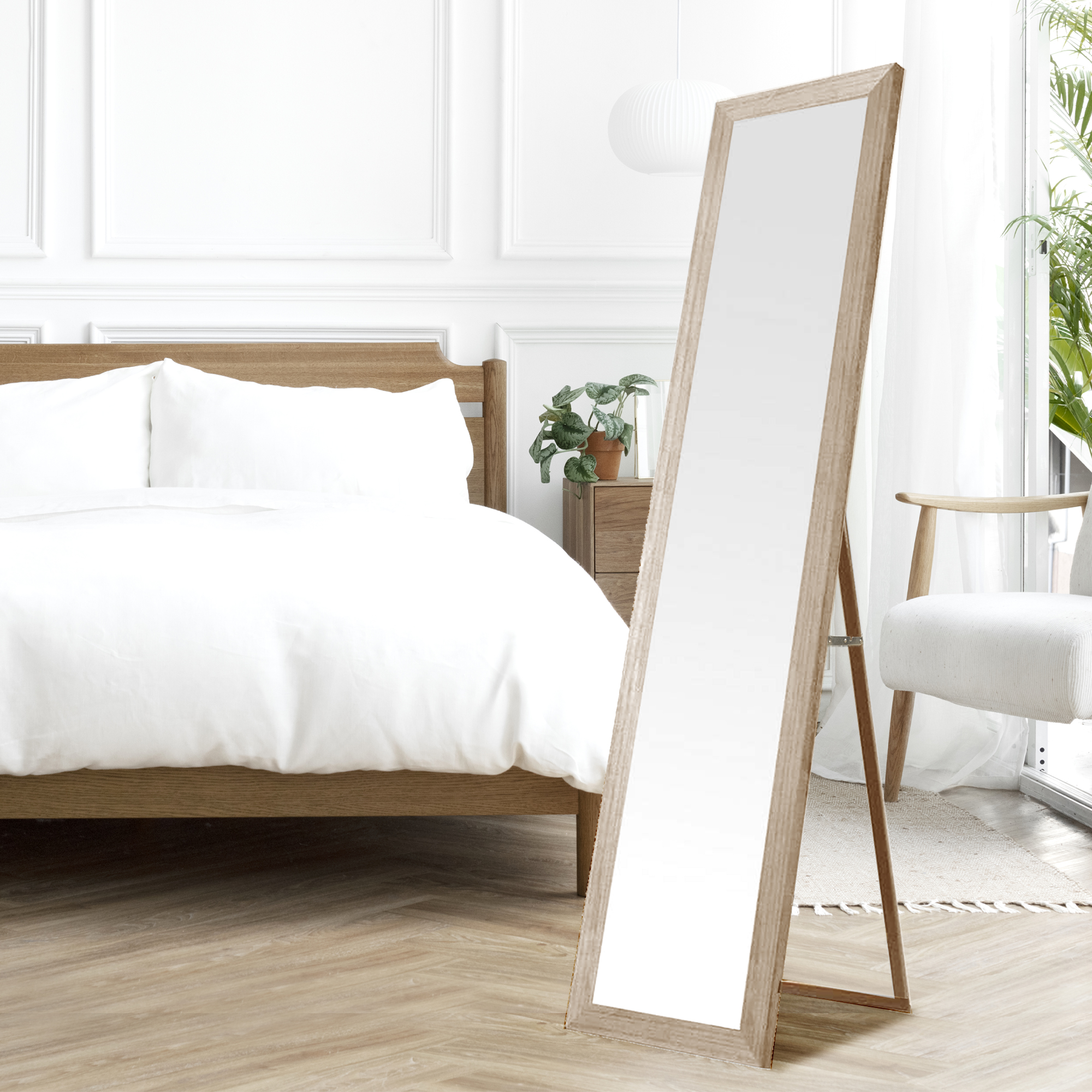 Un espejo de pie junto a una cama de madera con sábanas blancas.