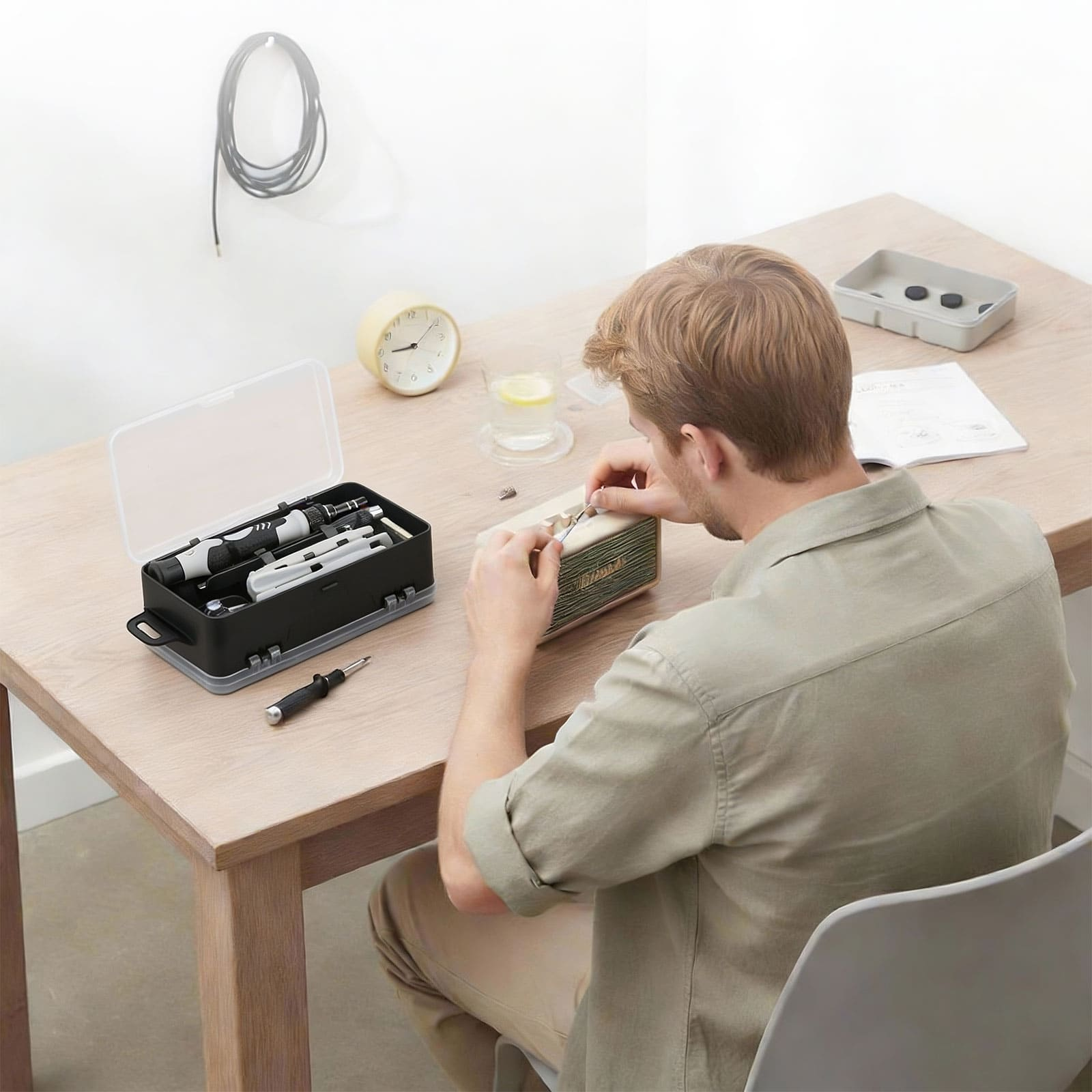 Hombre repara dispositivo, caja de herramientas y reloj en mesa.