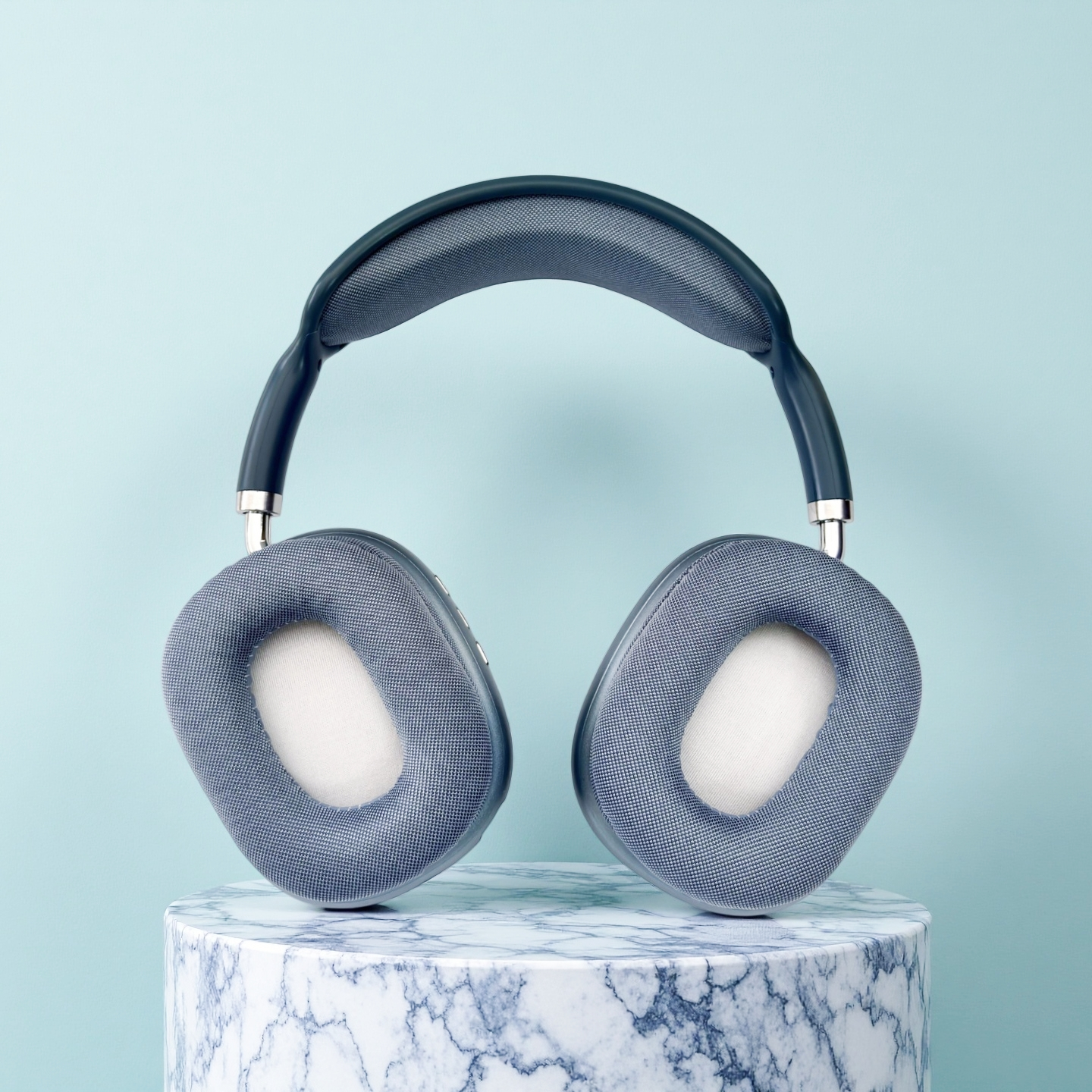 Auriculares grises con almohadillas blancas sobre pedestal de mármol, fondo azul.