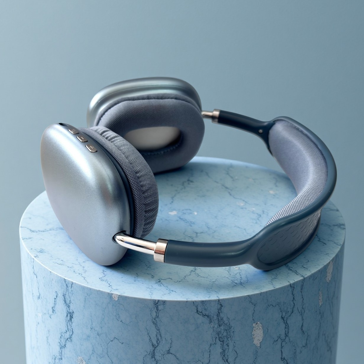 Auriculares plateados con almohadillas grises sobre un cilindro de mármol azul.