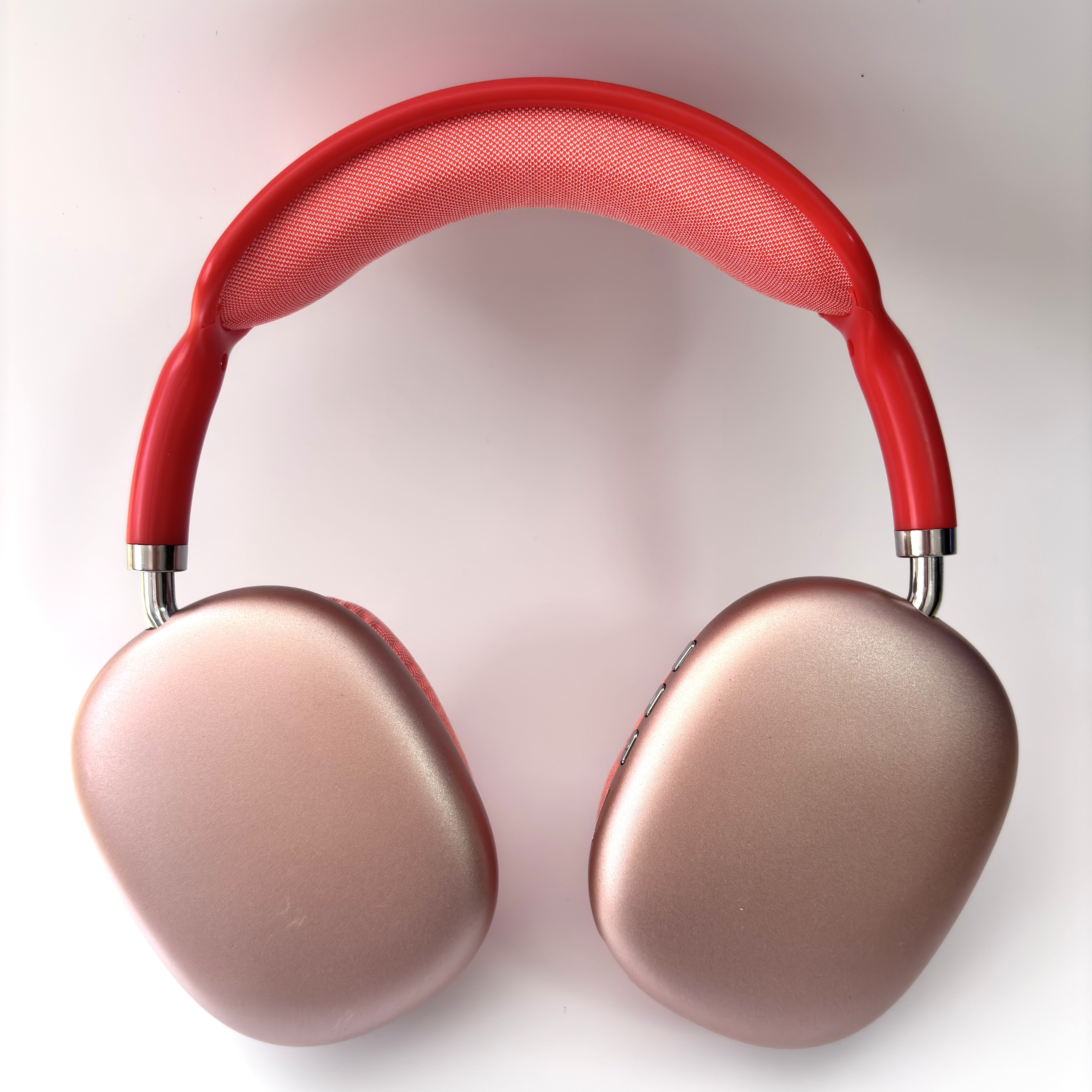Auriculares rojos y oro rosa con diadema de tela, sobre fondo blanco.