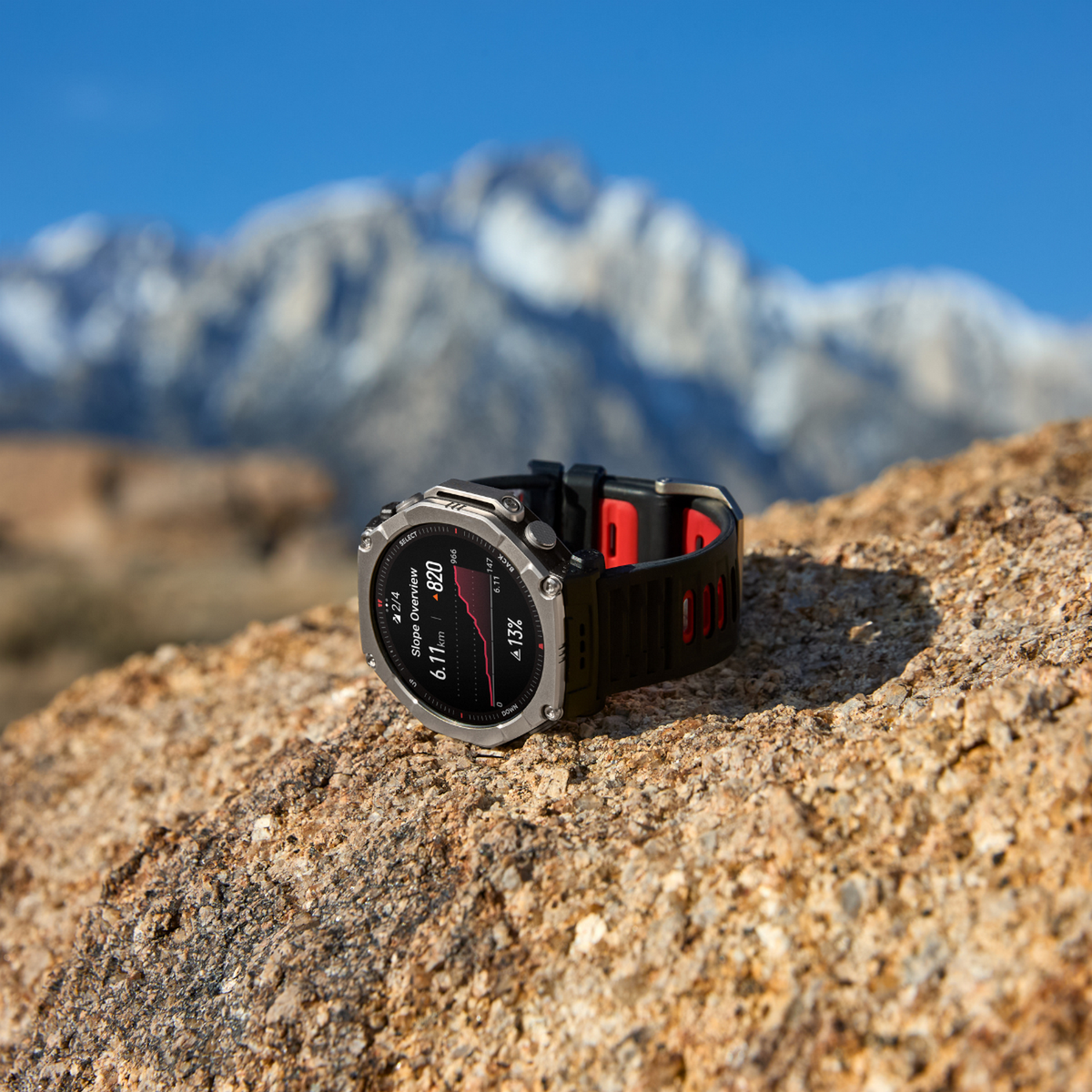 Eine silberne Smartwatch mit schwarzem und rotem Armband liegt auf einem Felsen.