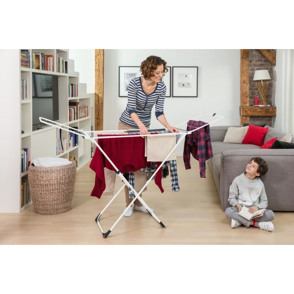 Kobieta wiesza pranie na suszarce, obok czyta dziecko.