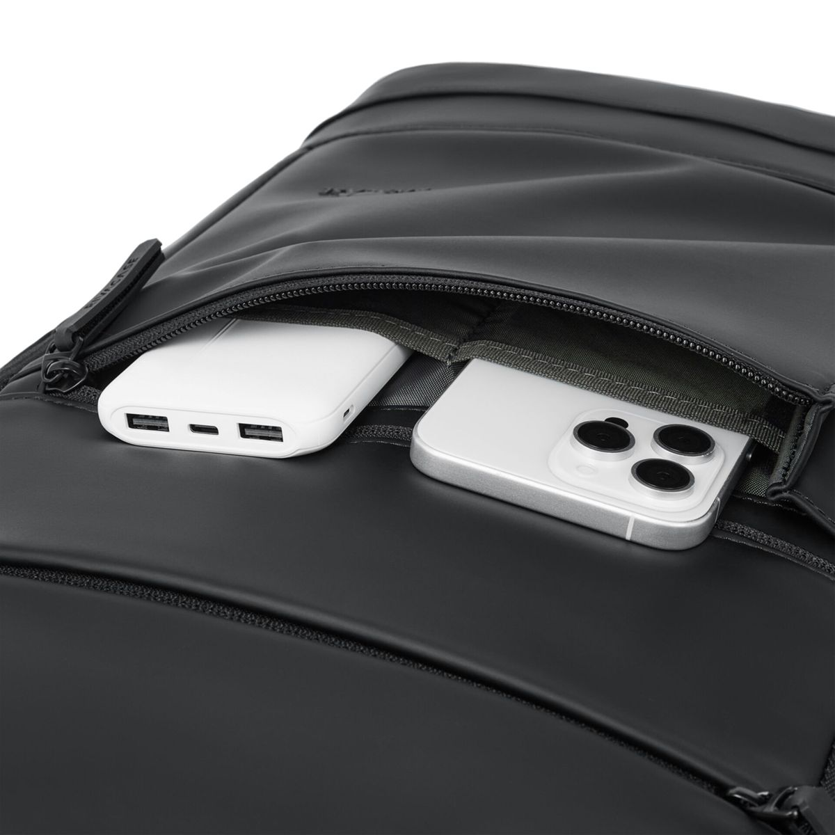 Biały power bank i srebrny smartfon znajdują się w otwartej kieszeni czarnego plecaka.