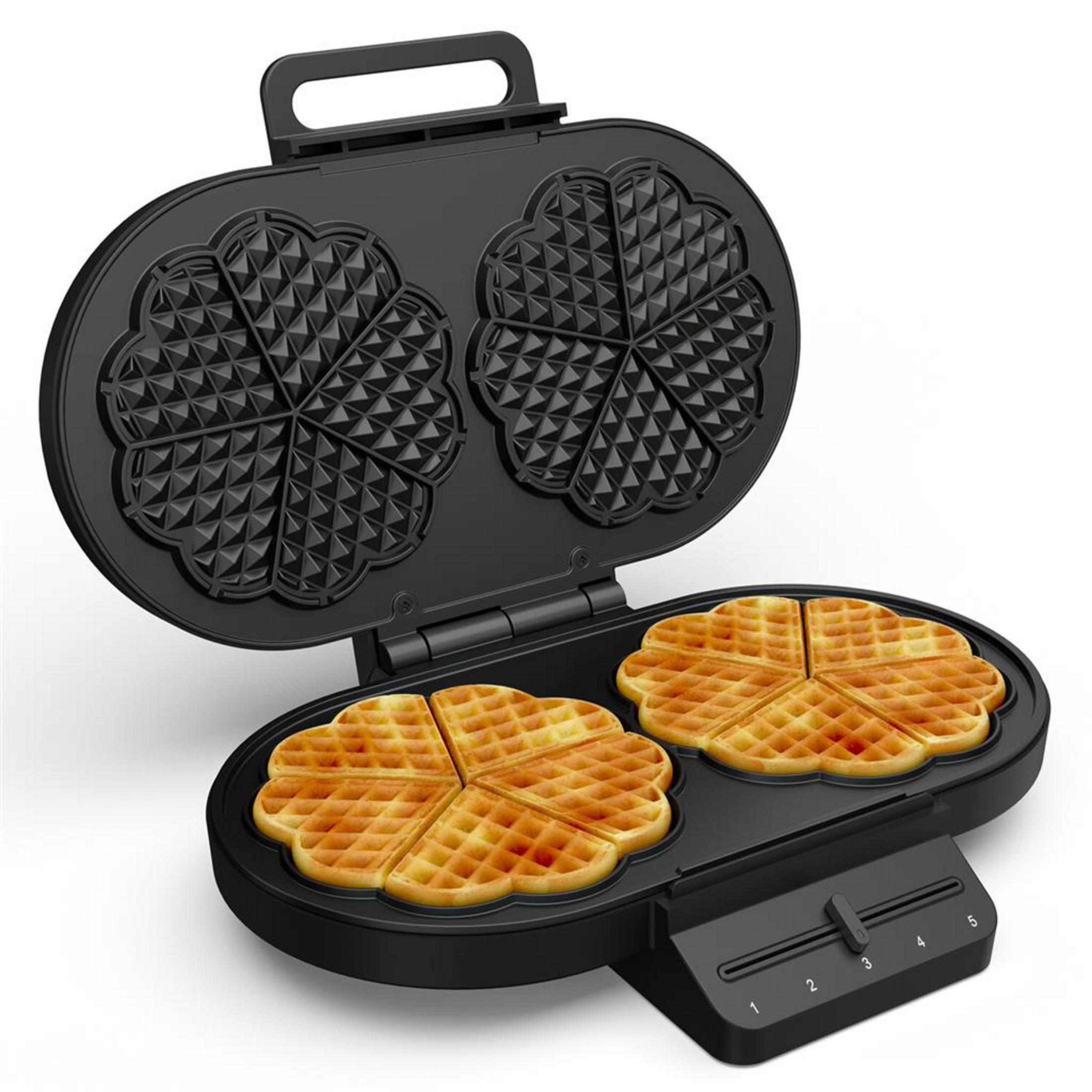 Una piastra per waffle nera aperta con due waffle a forma di cuore.