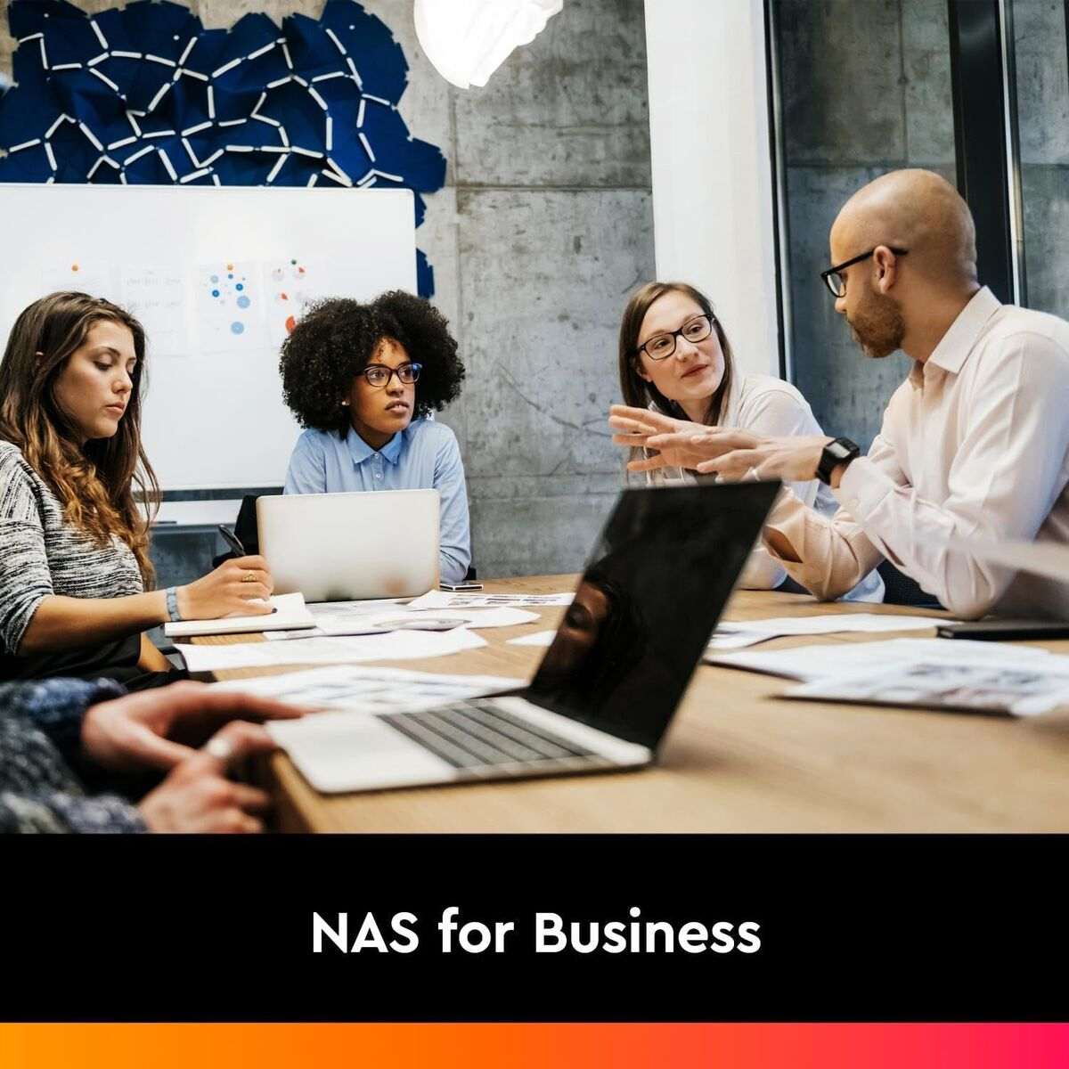 Cztery osoby dyskutują przy stole z laptopami i notatnikami.