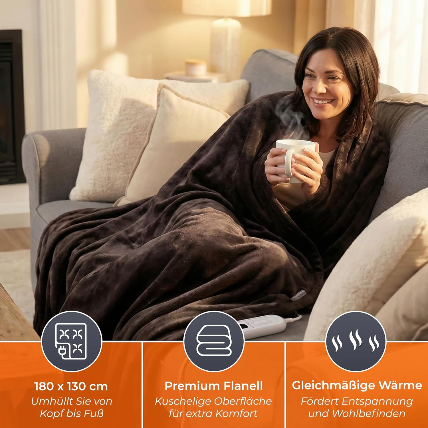 Eine Frau sitzt auf einem Sofa und hält eine Tasse, eingewickelt in eine Decke.