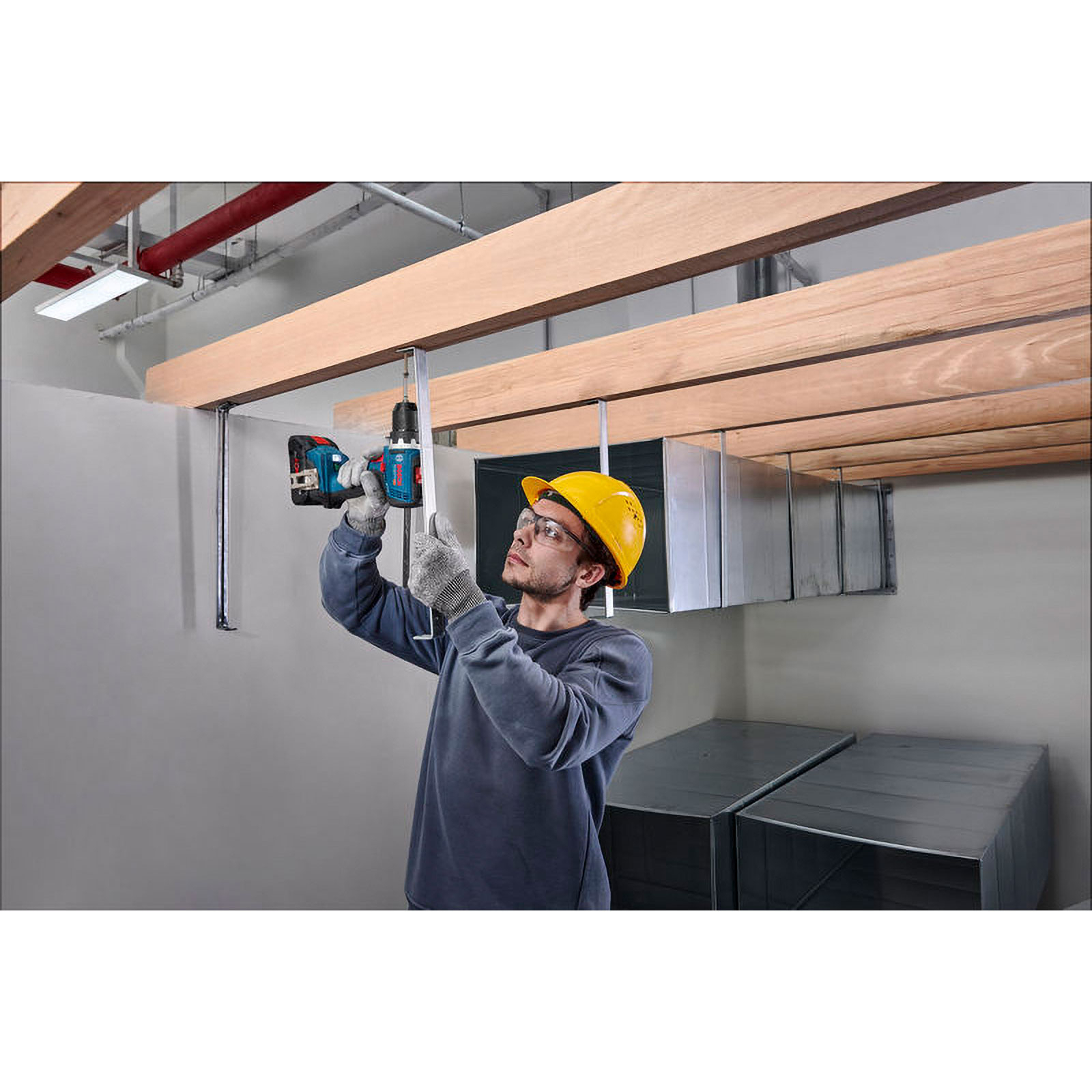Ein Mann mit Helm bohrt Holzdeckenbalken.