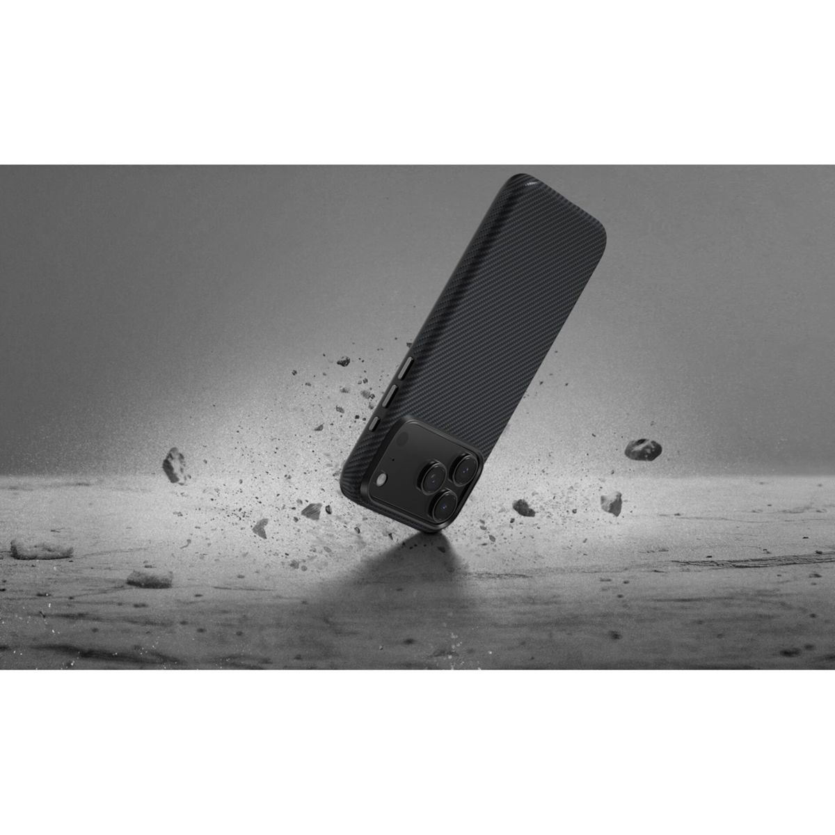 Ein schwarzes Handy mit Carbon-Muster fällt auf einen steinigen Boden.
