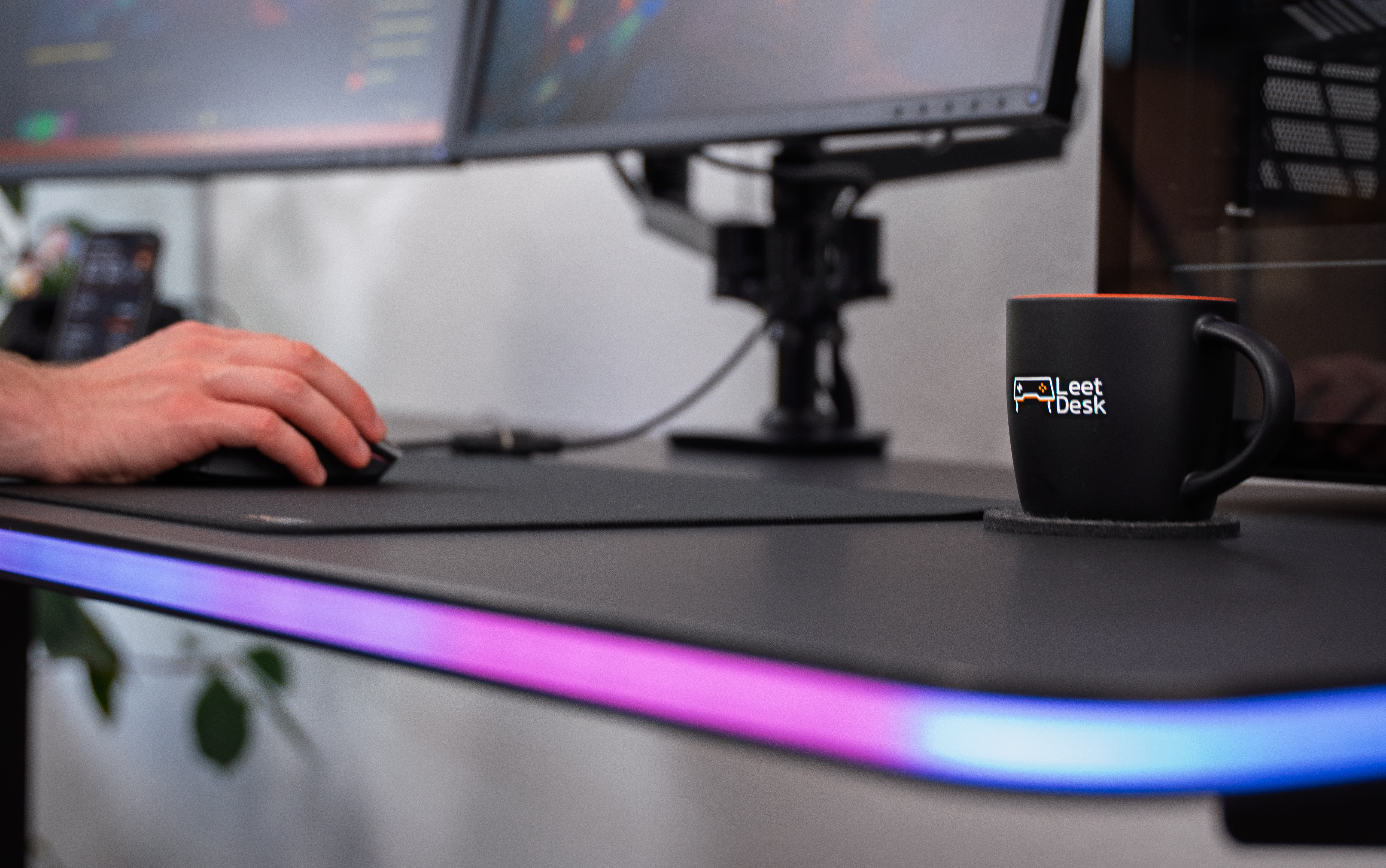 Ein Mann benutzt eine Maus auf einem Schreibtisch mit RGB-Beleuchtung. Daneben steht eine Tasse.