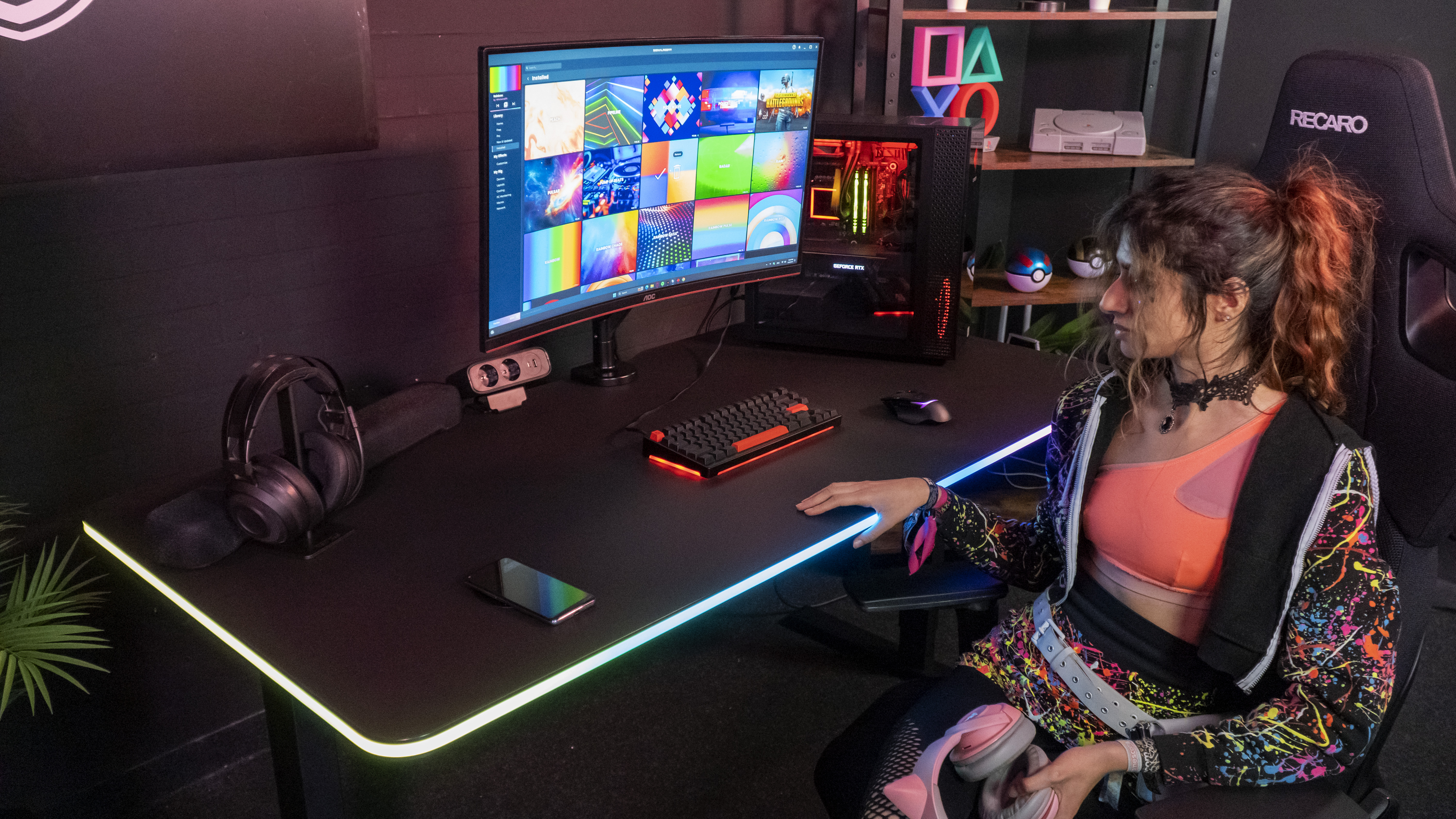 Eine Frau sitzt an einem Schreibtisch mit einem Gaming-PC, Monitor, Tastatur und Maus.