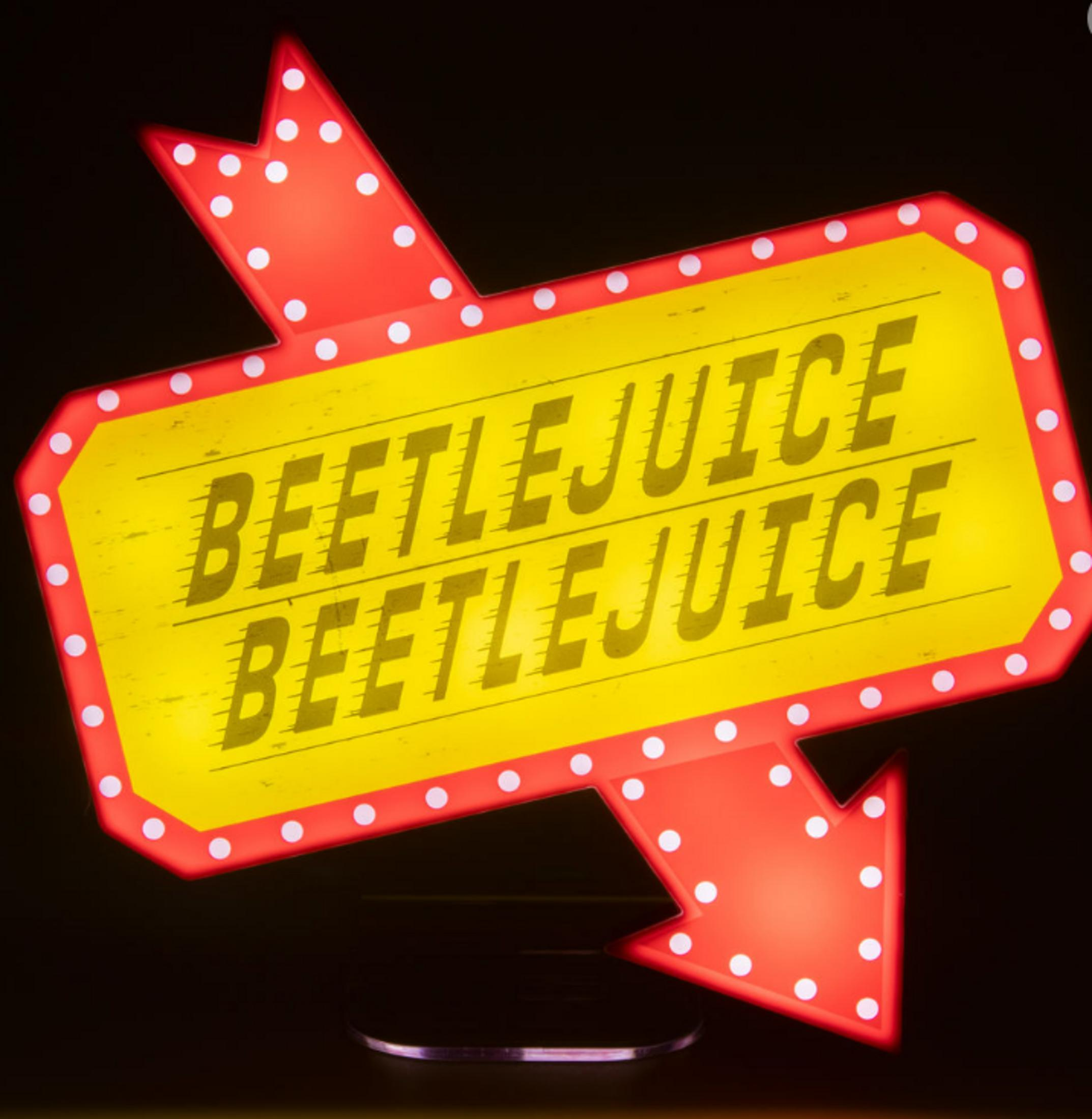 Eine gelbe Leuchtreklame mit roten Pfeilen zeigt 'BEETLEJUICE' zweimal.