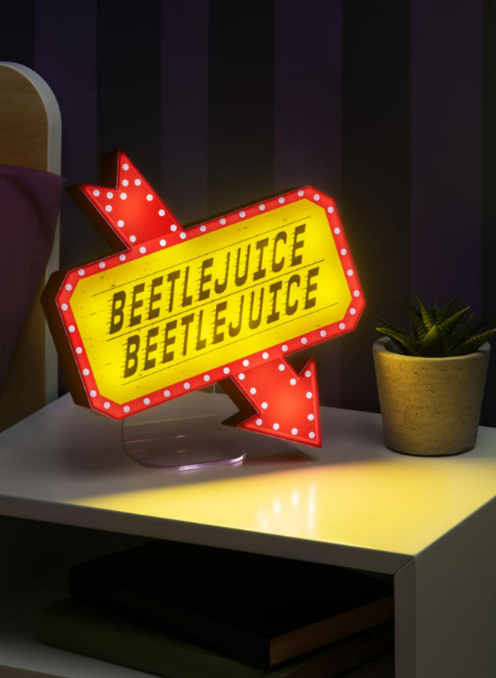 Beetlejuice Leuchtreklame auf Nachttisch neben Topfpflanze.