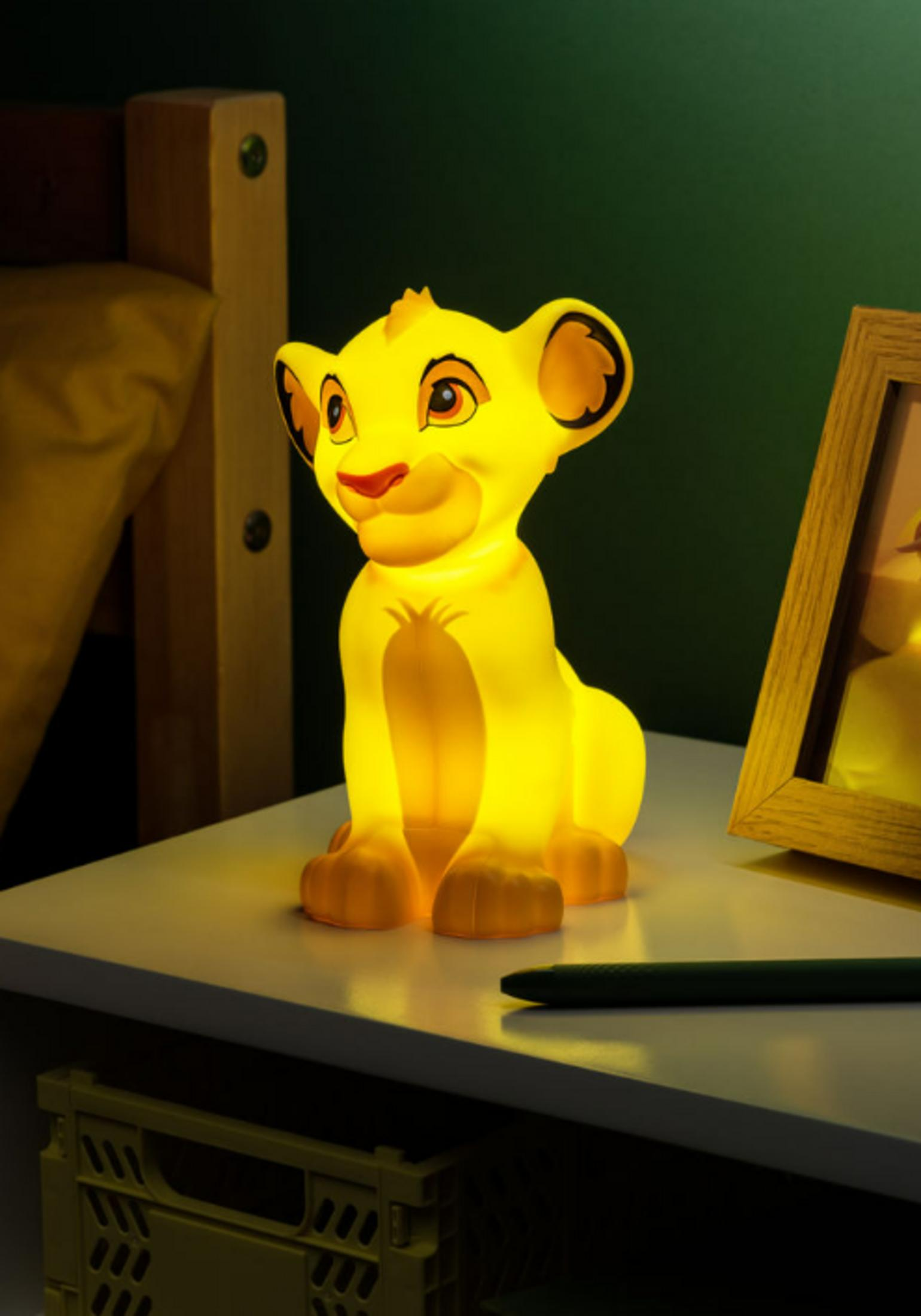 Gelbe Löwenfigur-Lampe auf Nachttisch, neben Bilderrahmen und Stift.