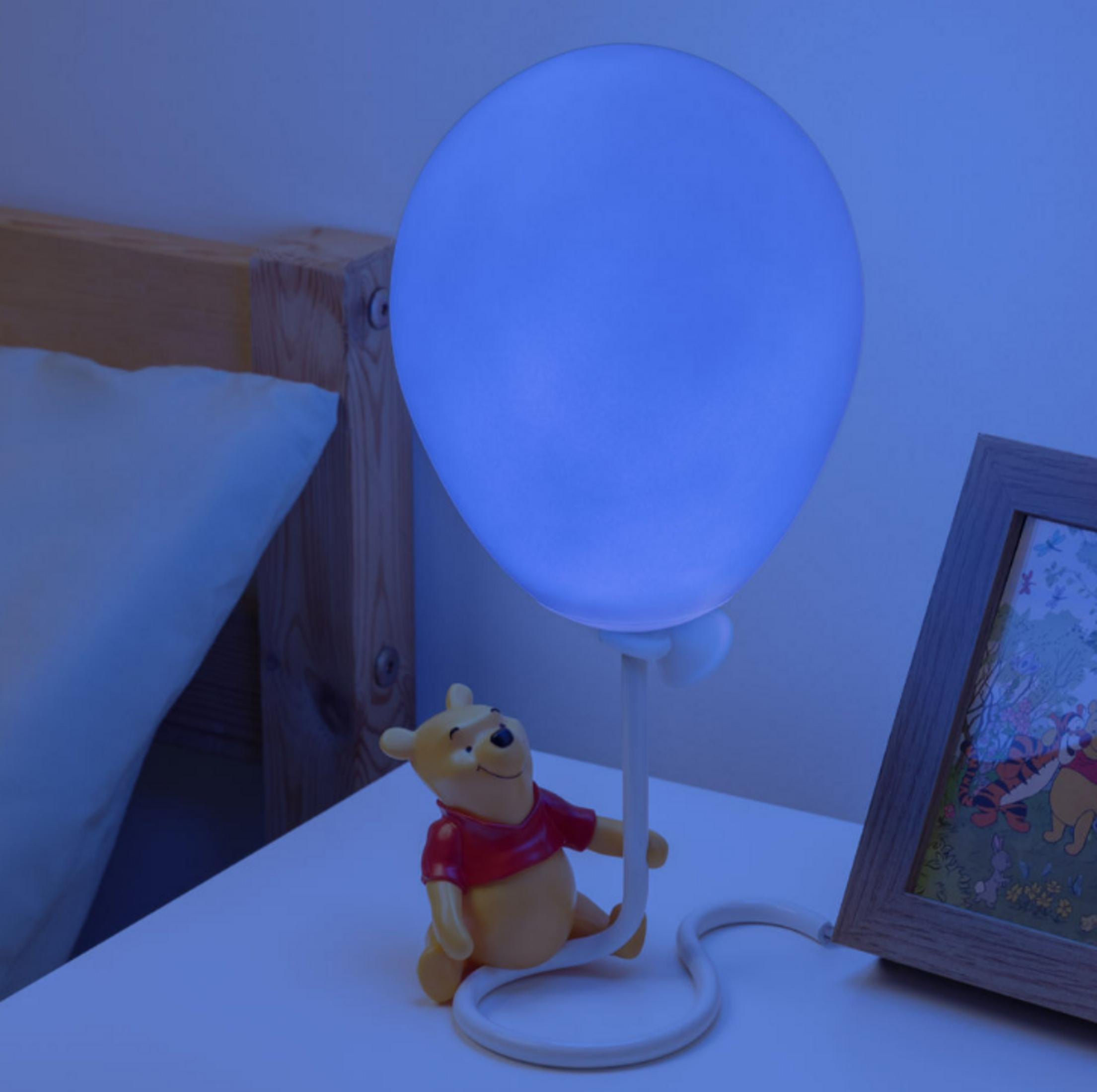 Ein Winnie Puuh Lampenfuß mit blau beleuchtetem Ballon auf Nachttisch.