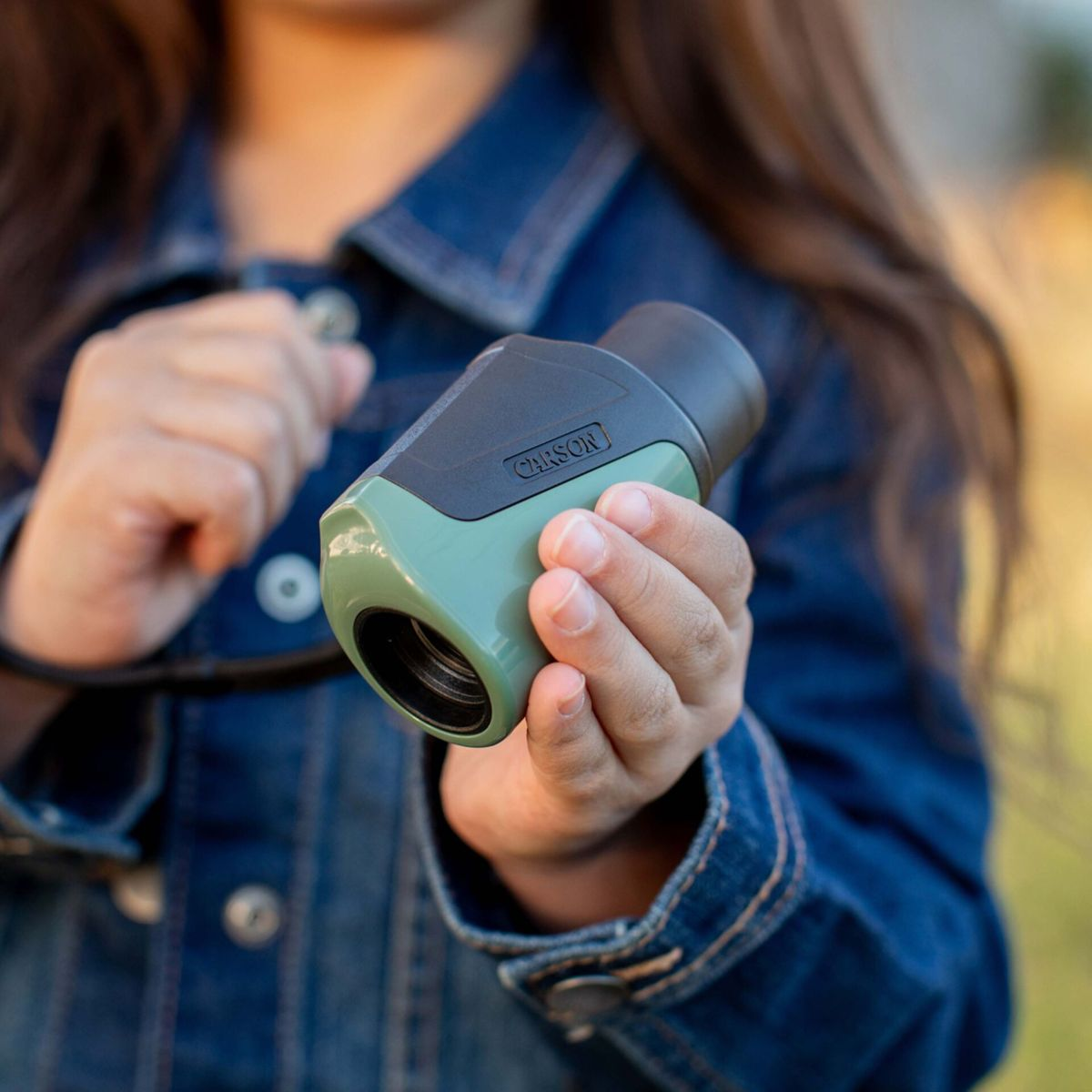 Un bambino con giacca di jeans tiene un binocolo verde con impugnatura nera.