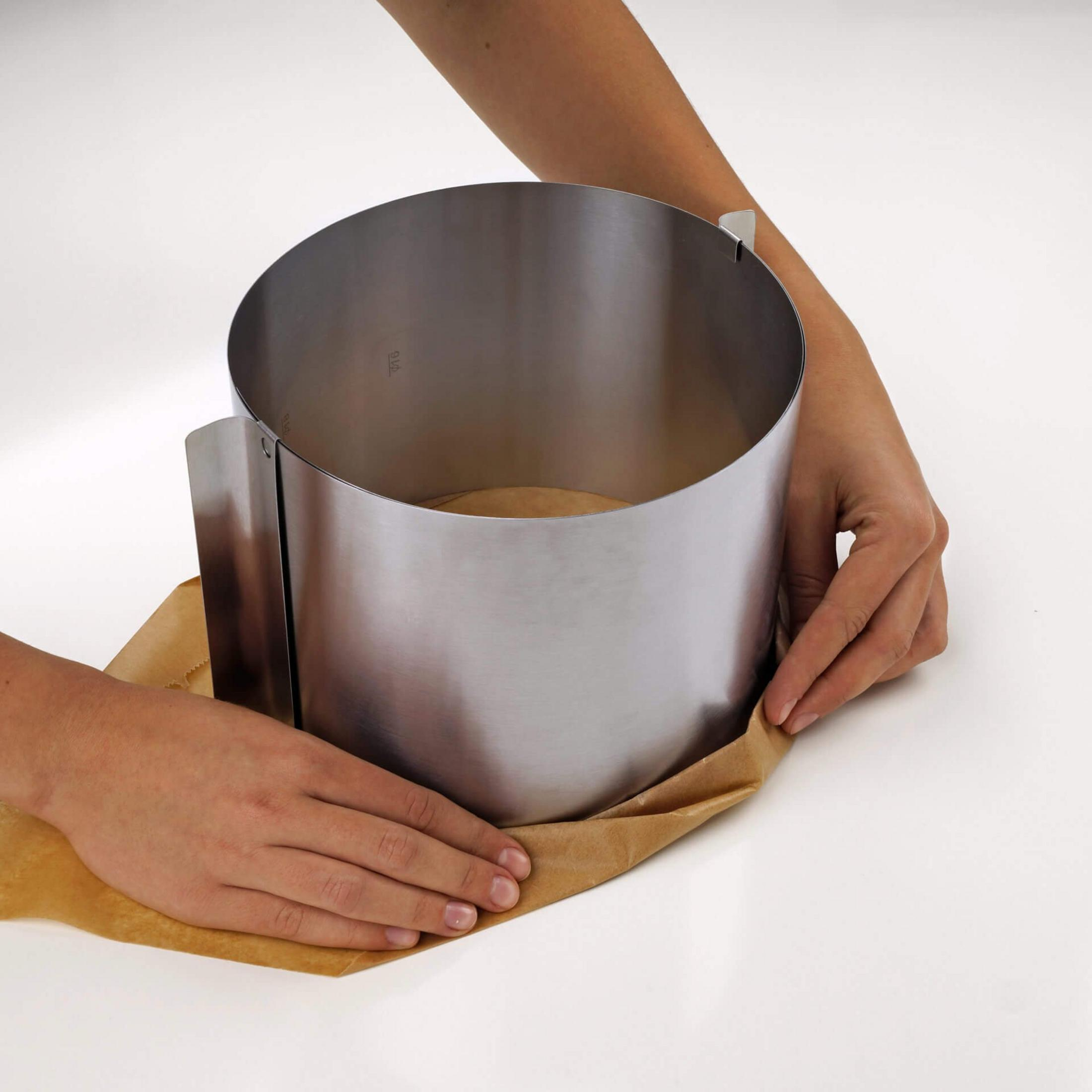 Hände legen Backpapier unter einen Metallring auf weißem Tisch.