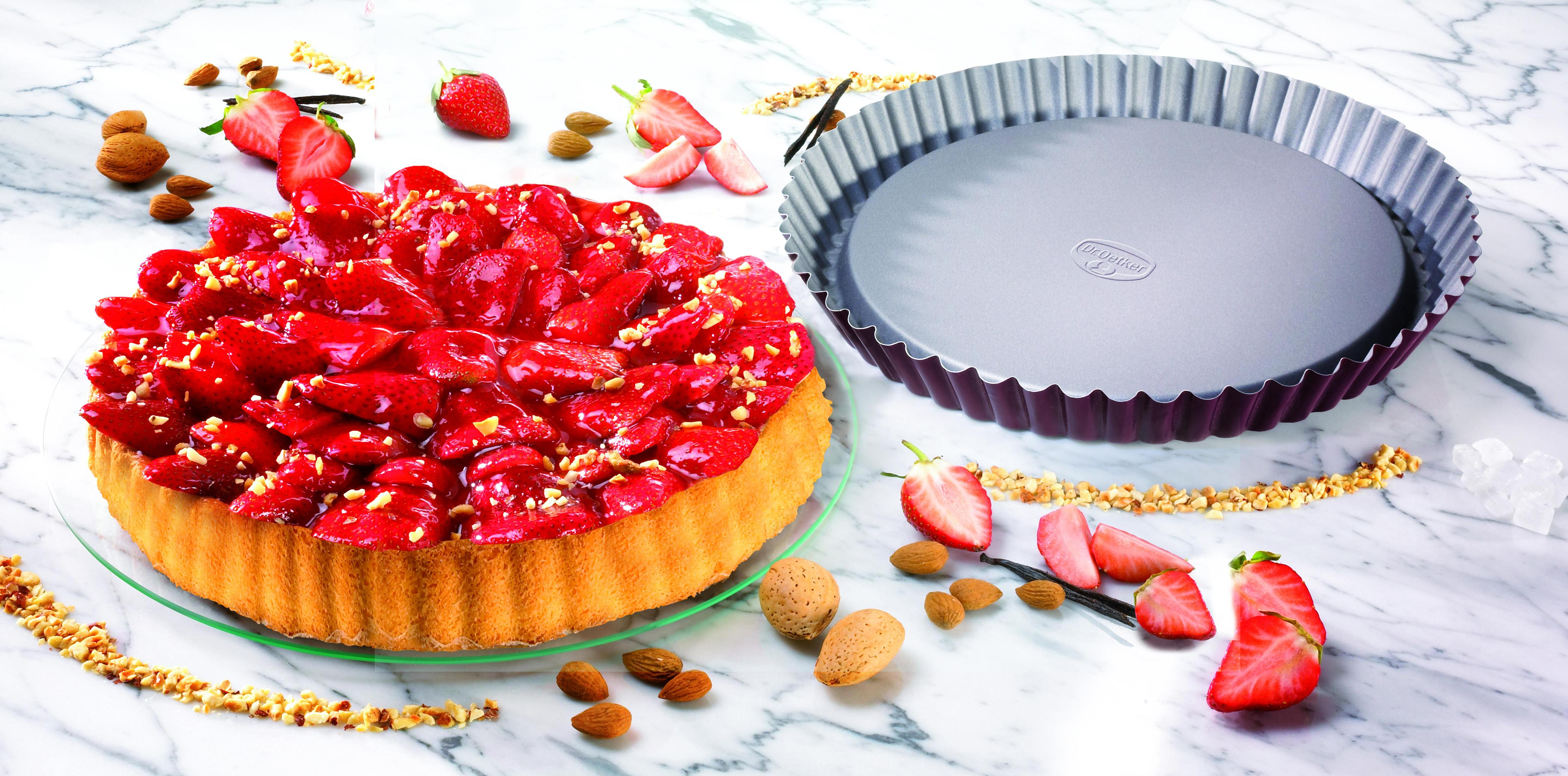 Erdbeertorte mit Nüssen und eine leere Kuchenform auf Marmor.