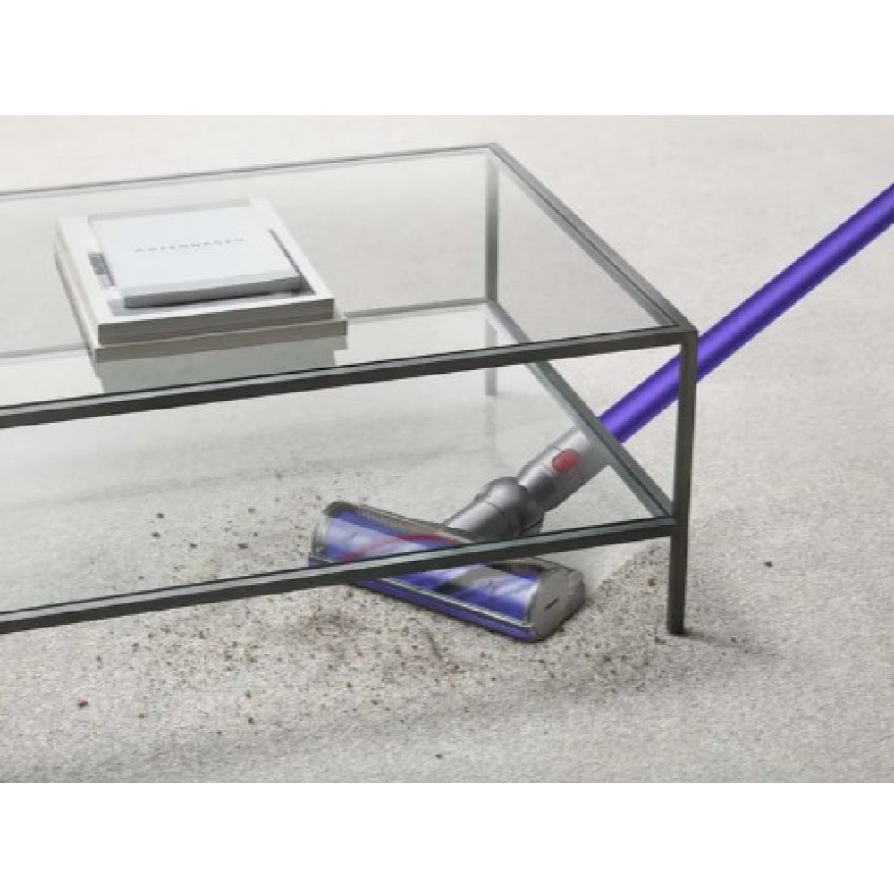 Fioletowy odkurzacz czyści zakurzoną podłogę pod szklanym stolikiem.