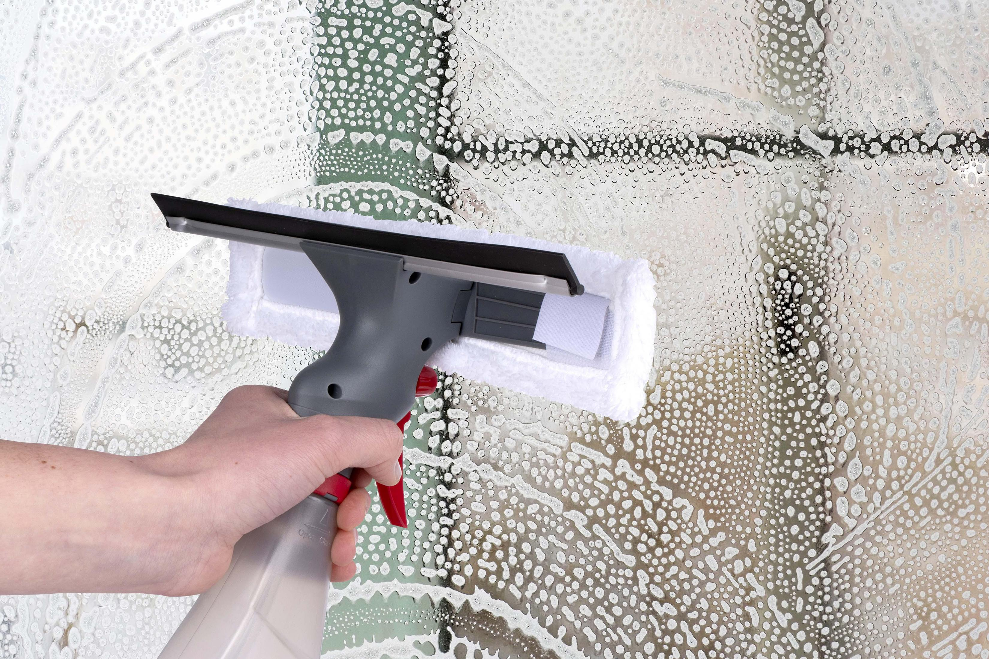 Una mano spruzza acqua saponata su una finestra coperta di bolle.