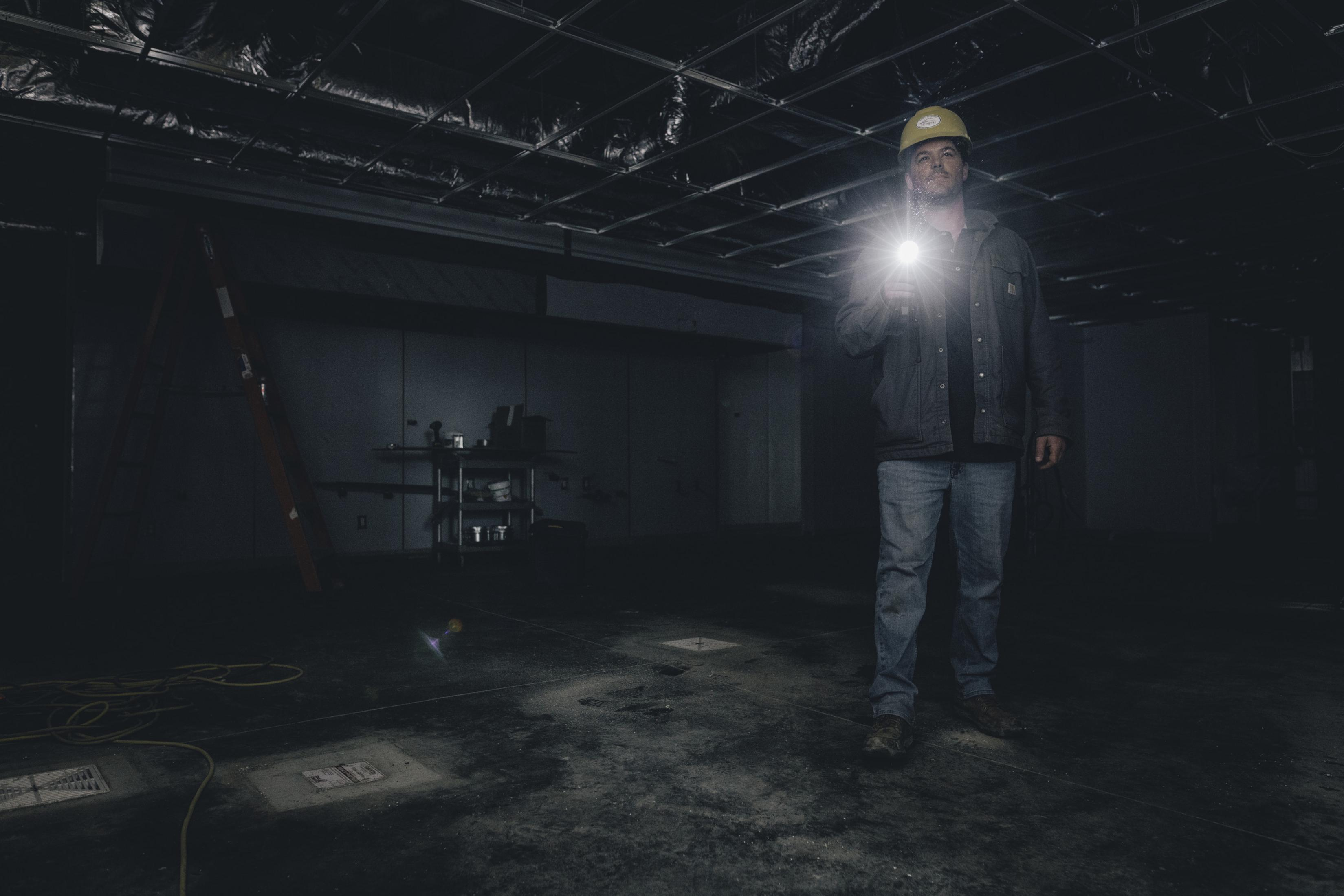 Ein Mann mit Helm leuchtet mit einer Taschenlampe in einem dunklen Raum.
