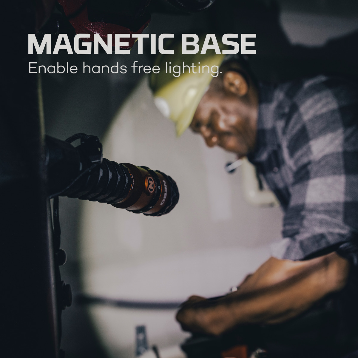 Ein Mann mit Helm und kariertem Hemd arbeitet, eine magnetische Lampe ist befestigt.