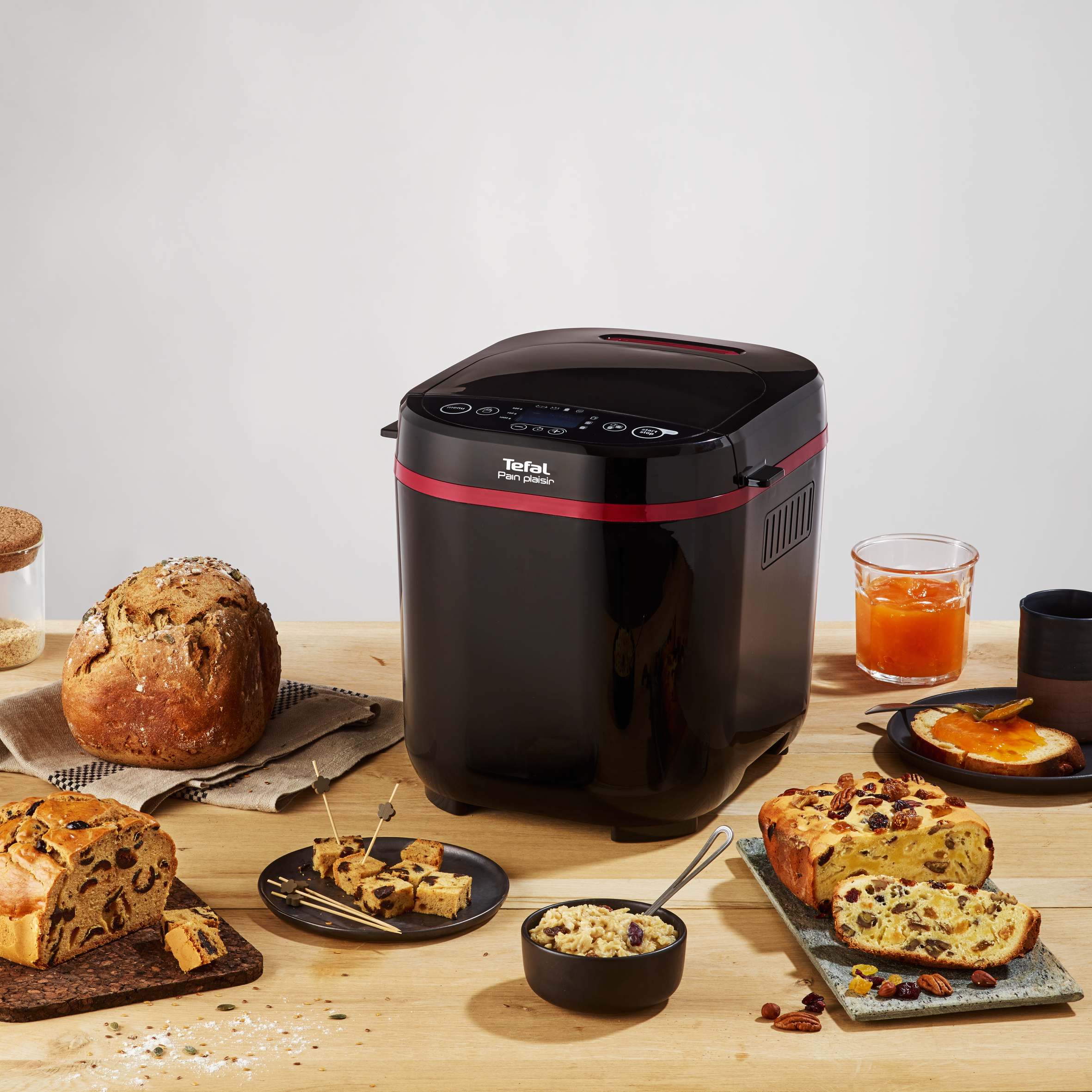 Brotbackautomat mit Brot, Kuchen und Marmelade auf Holztisch.