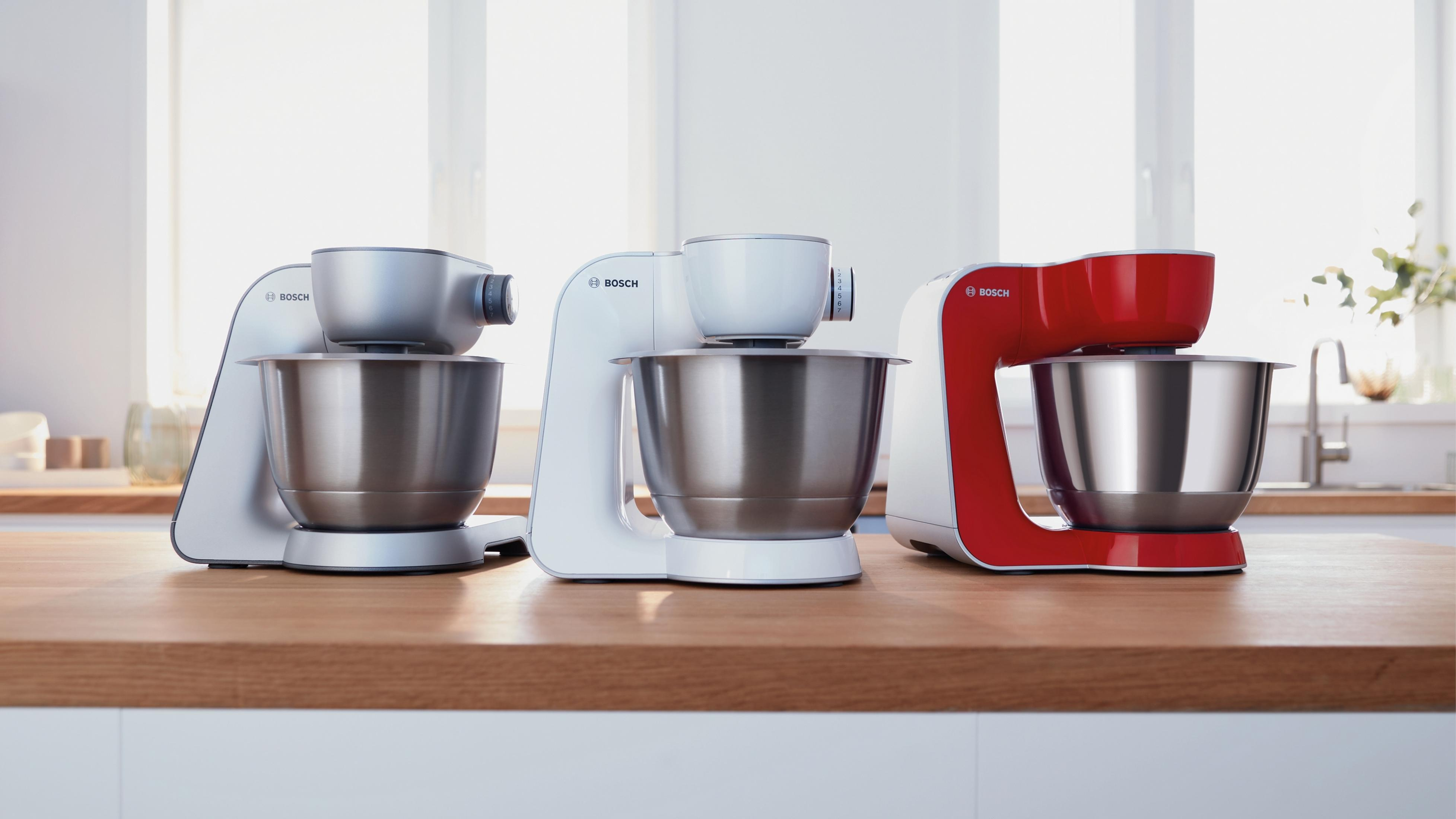 Tre impastatrici Bosch su un bancone di legno: modelli bianco, argento e rosso.