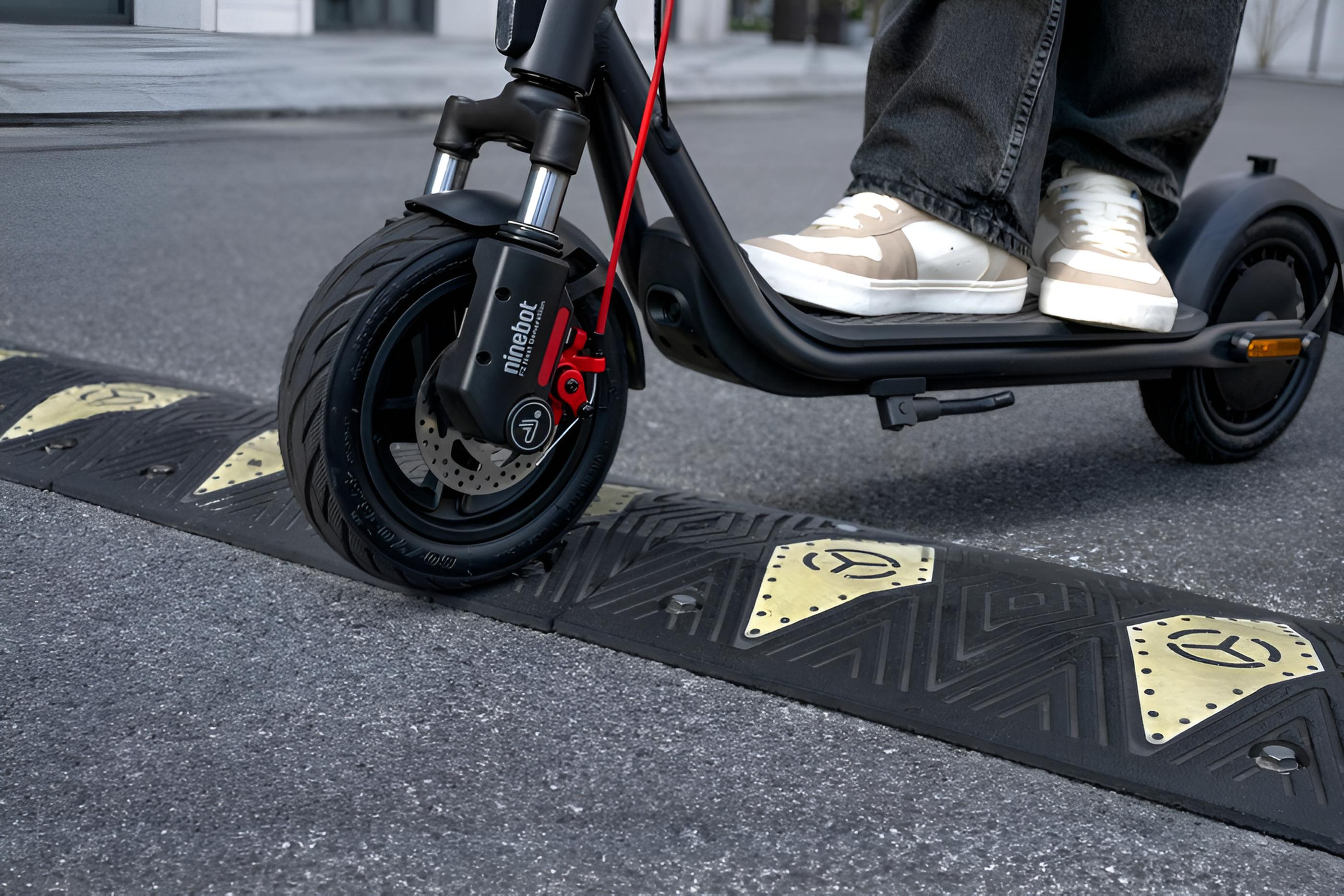 Uno scooter elettrico passa su un dosso nero con segnaletica gialla.