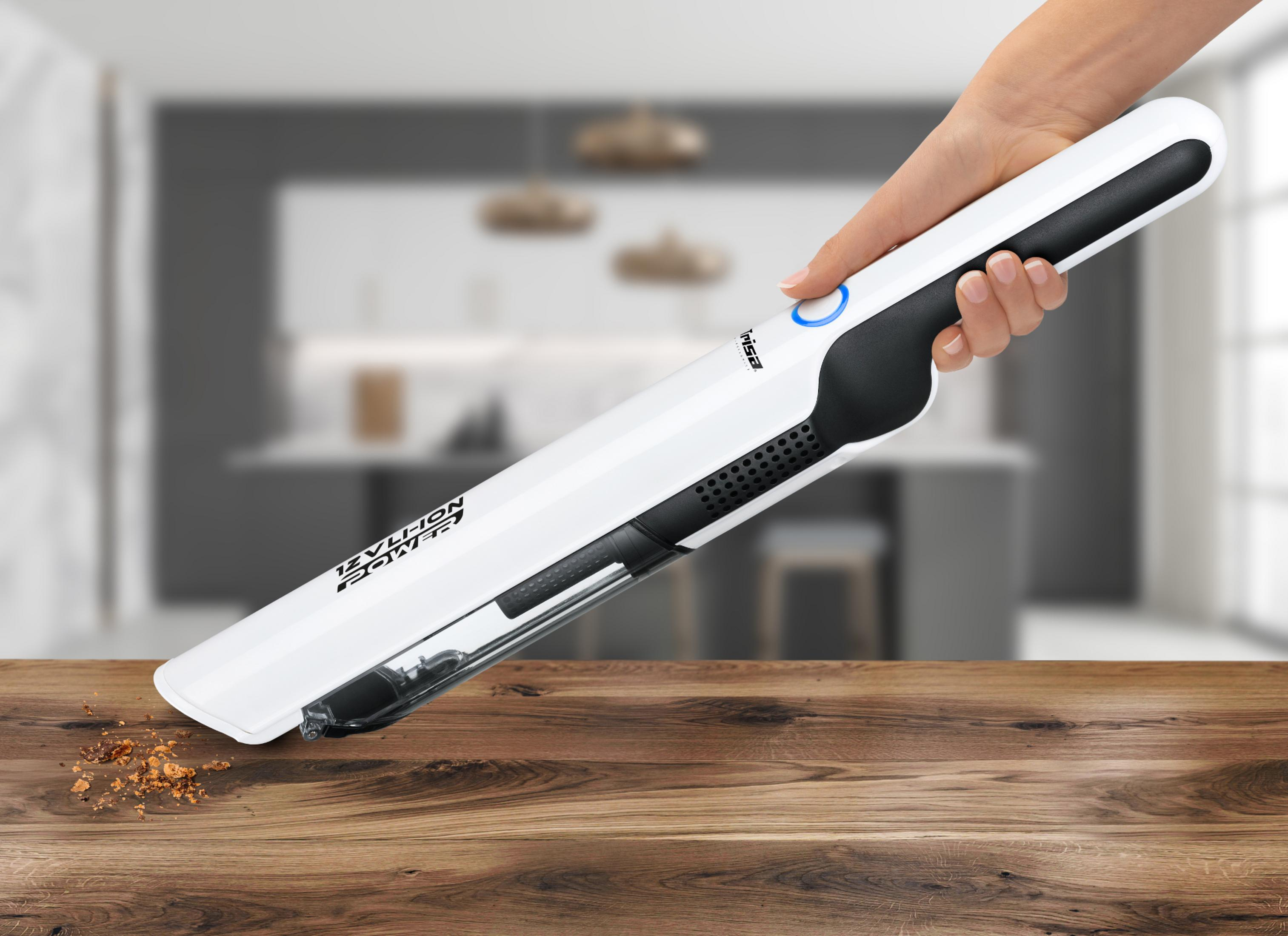 Una mano tiene un aspirapolvere portatile bianco che aspira briciole da un tavolo di legno.