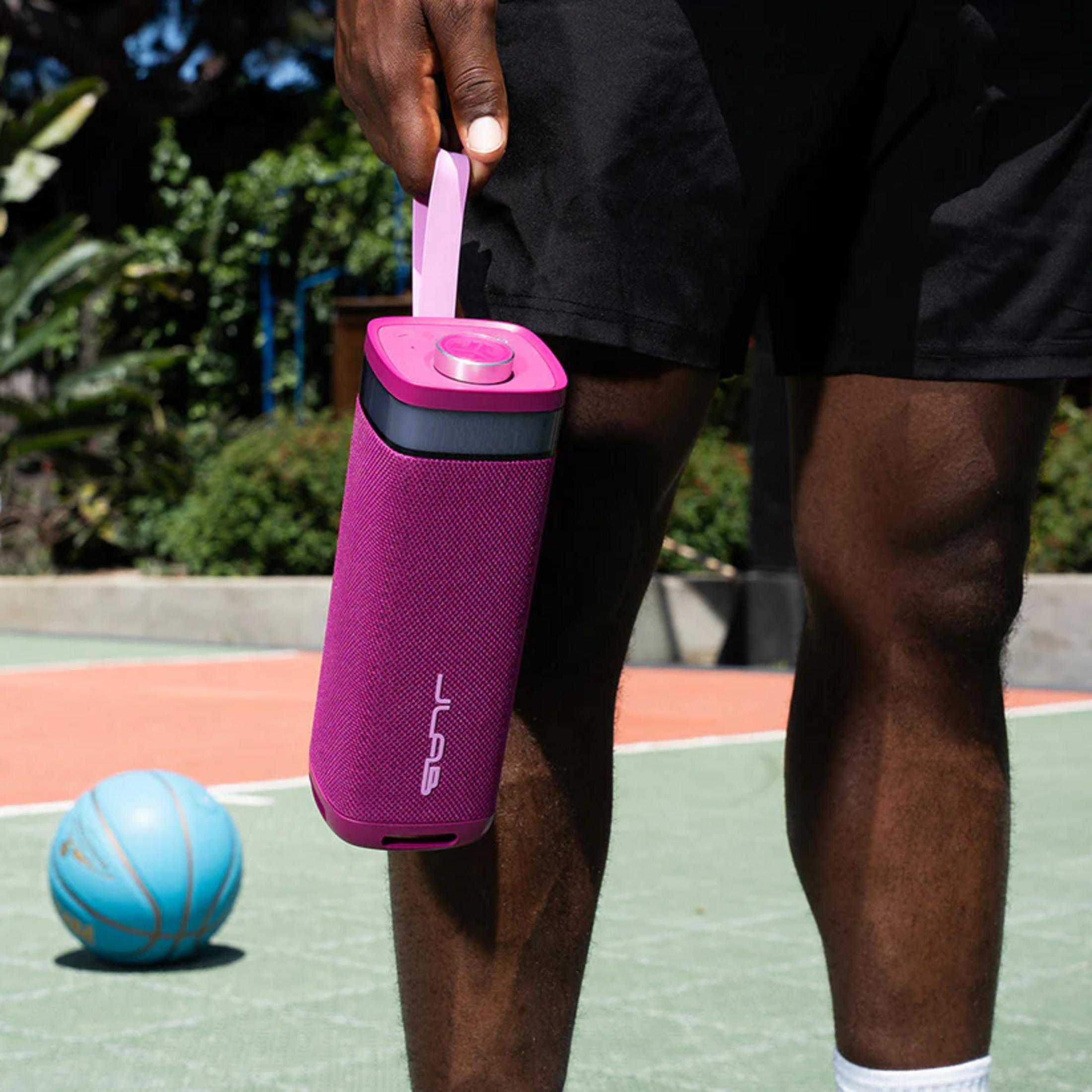 Un homme tient une enceinte violette. Un ballon de basket bleu repose au sol.