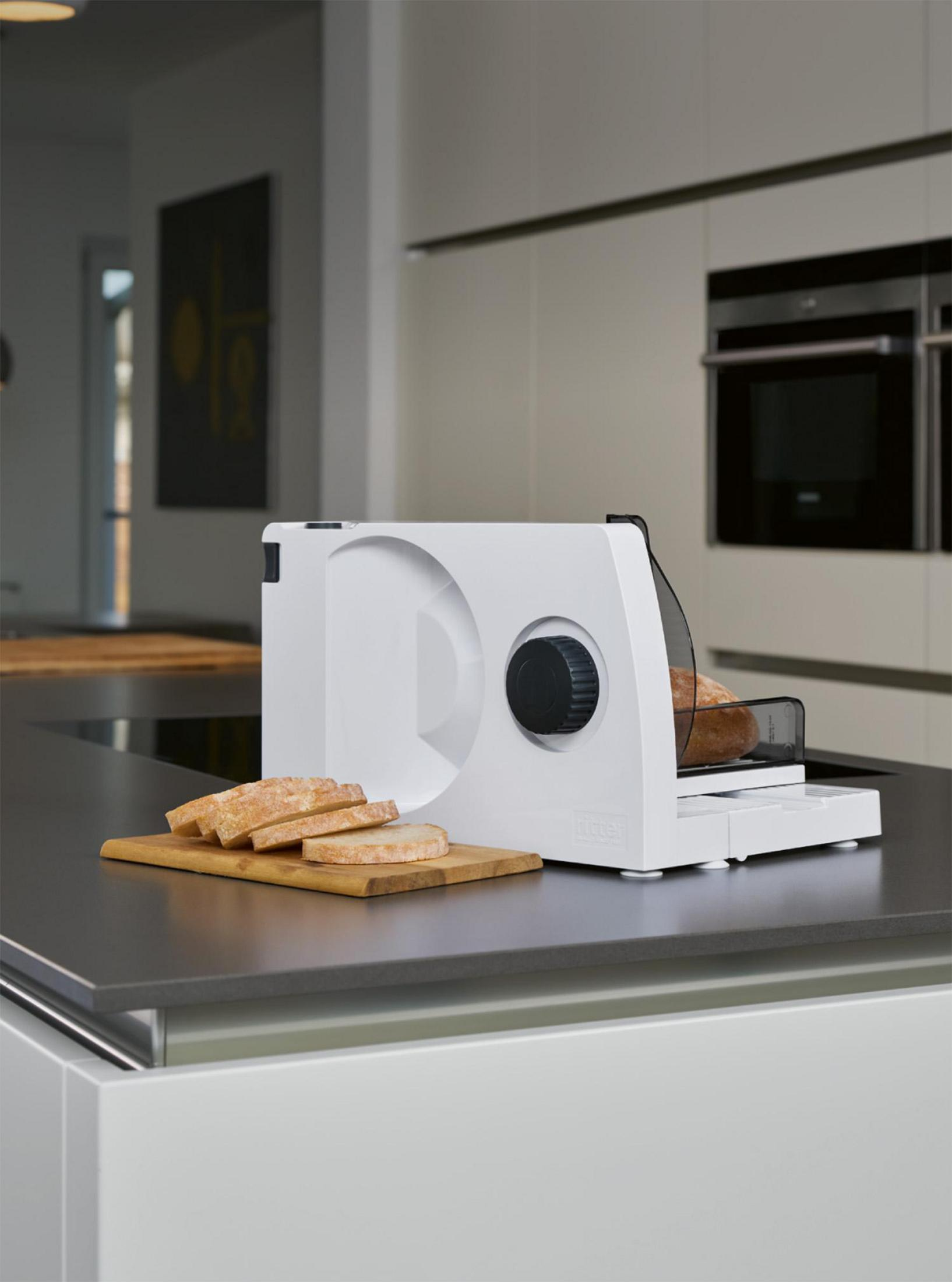 Un'affettatrice per pane bianca con pane affettato su un tagliere di legno in una cucina moderna.
