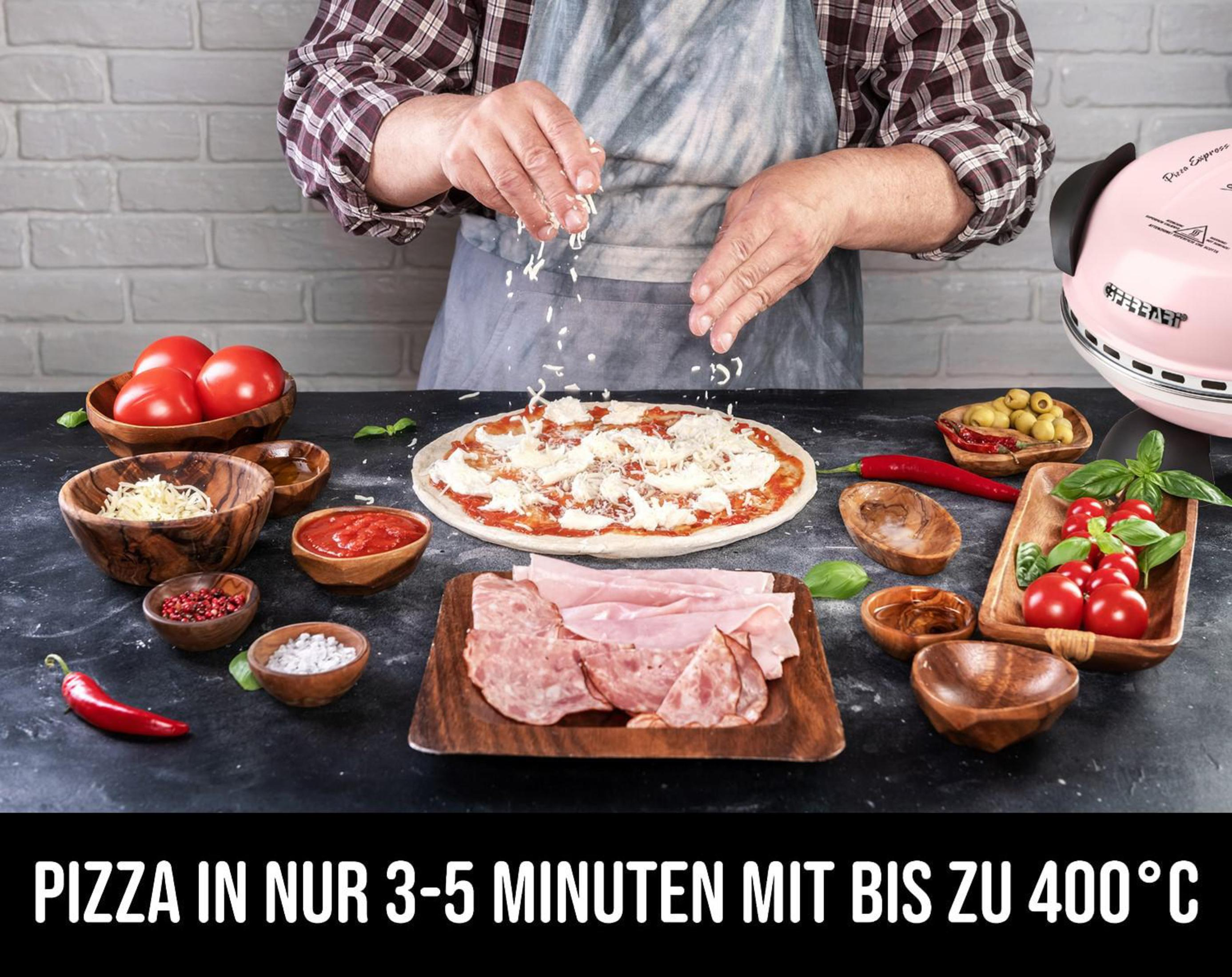 Mann bestreut Pizza mit geriebenem Käse. Zutaten wie Tomaten, Oliven und Schinken liegen daneben.