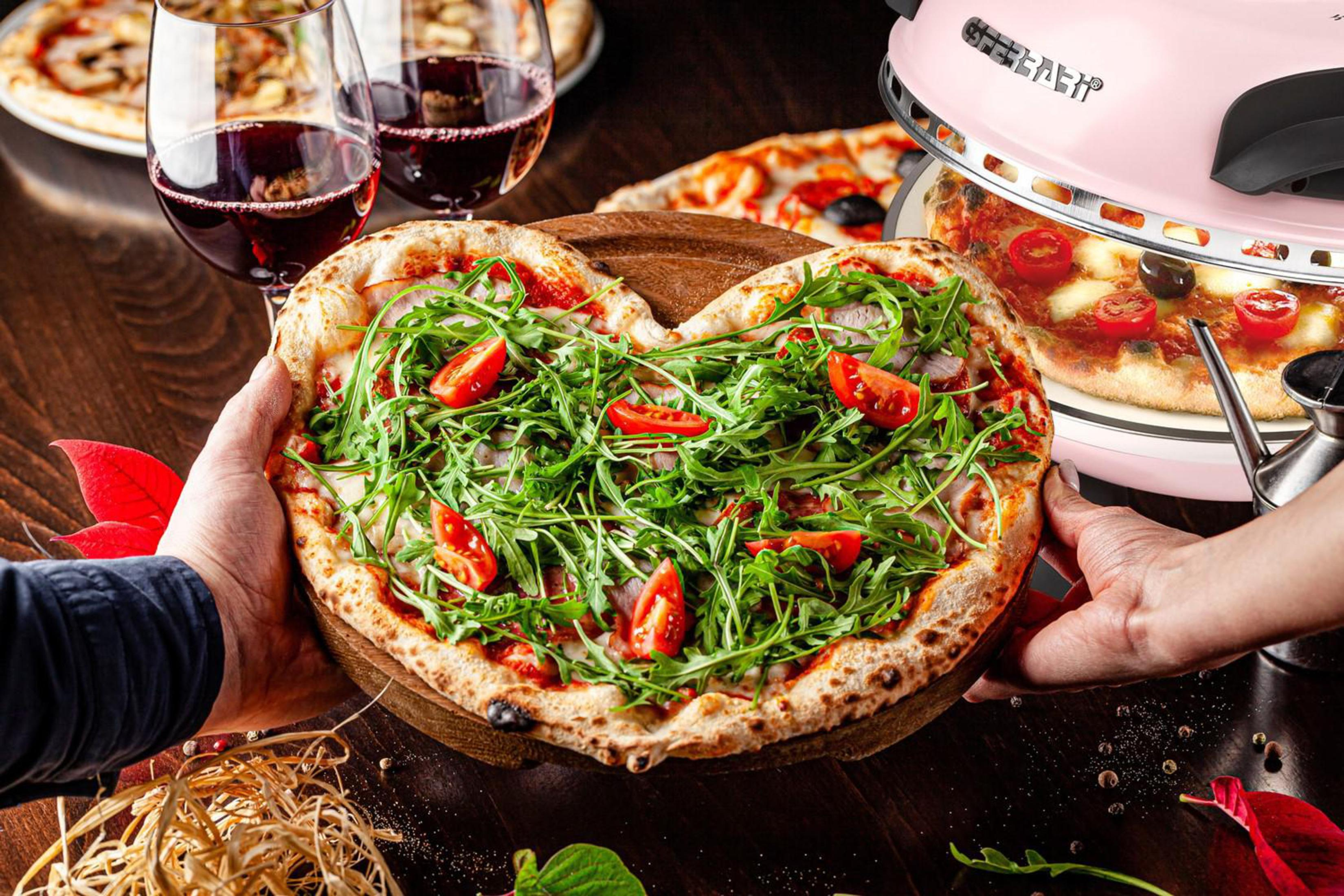 Herzförmige Pizza mit Rucola und Tomaten, von Händen gehalten, mit Wein und rosa Pizzaofen.