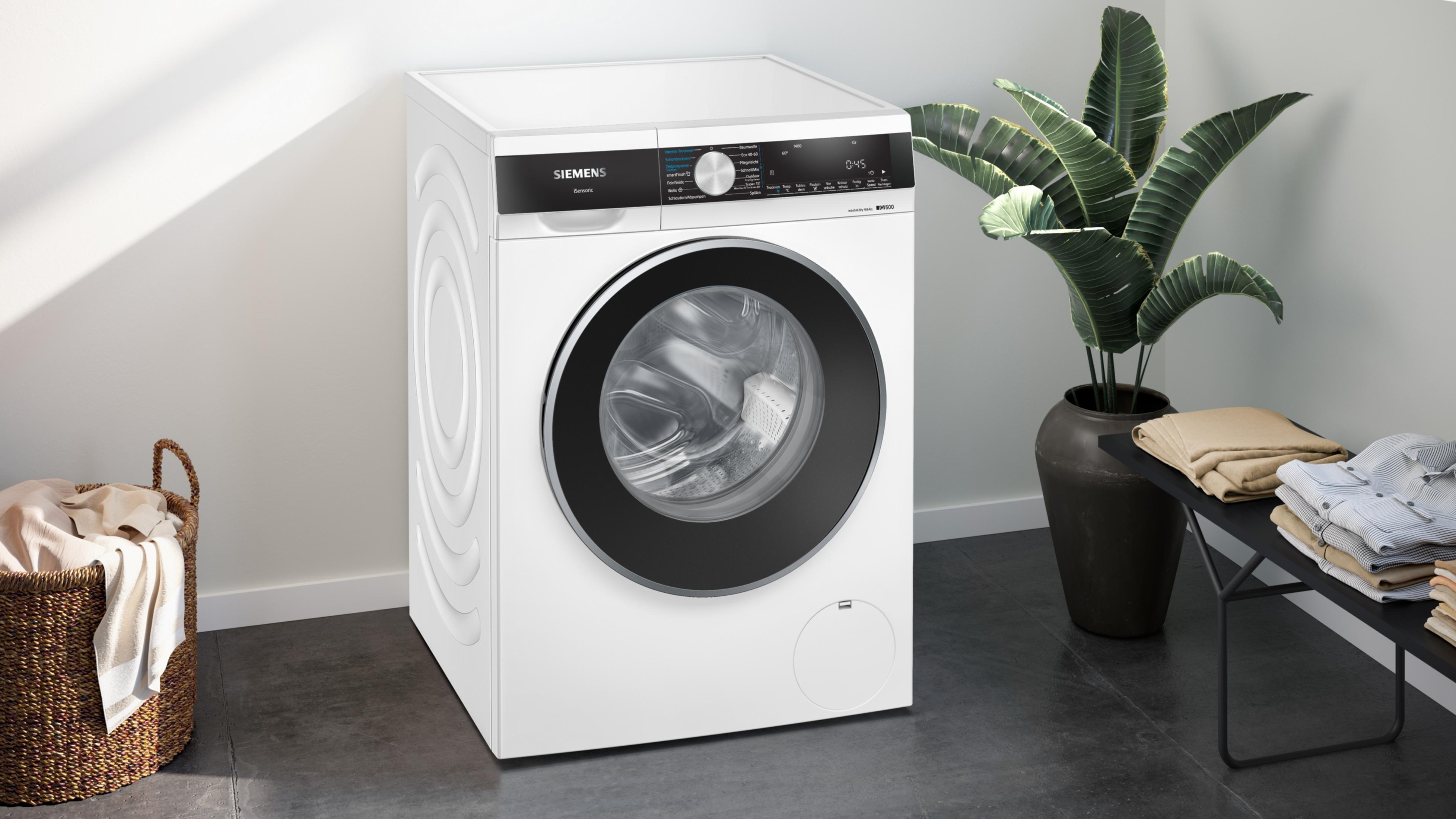 Weiße Siemens Waschmaschine mit schwarzer Tür und Pflanzen im Hintergrund.