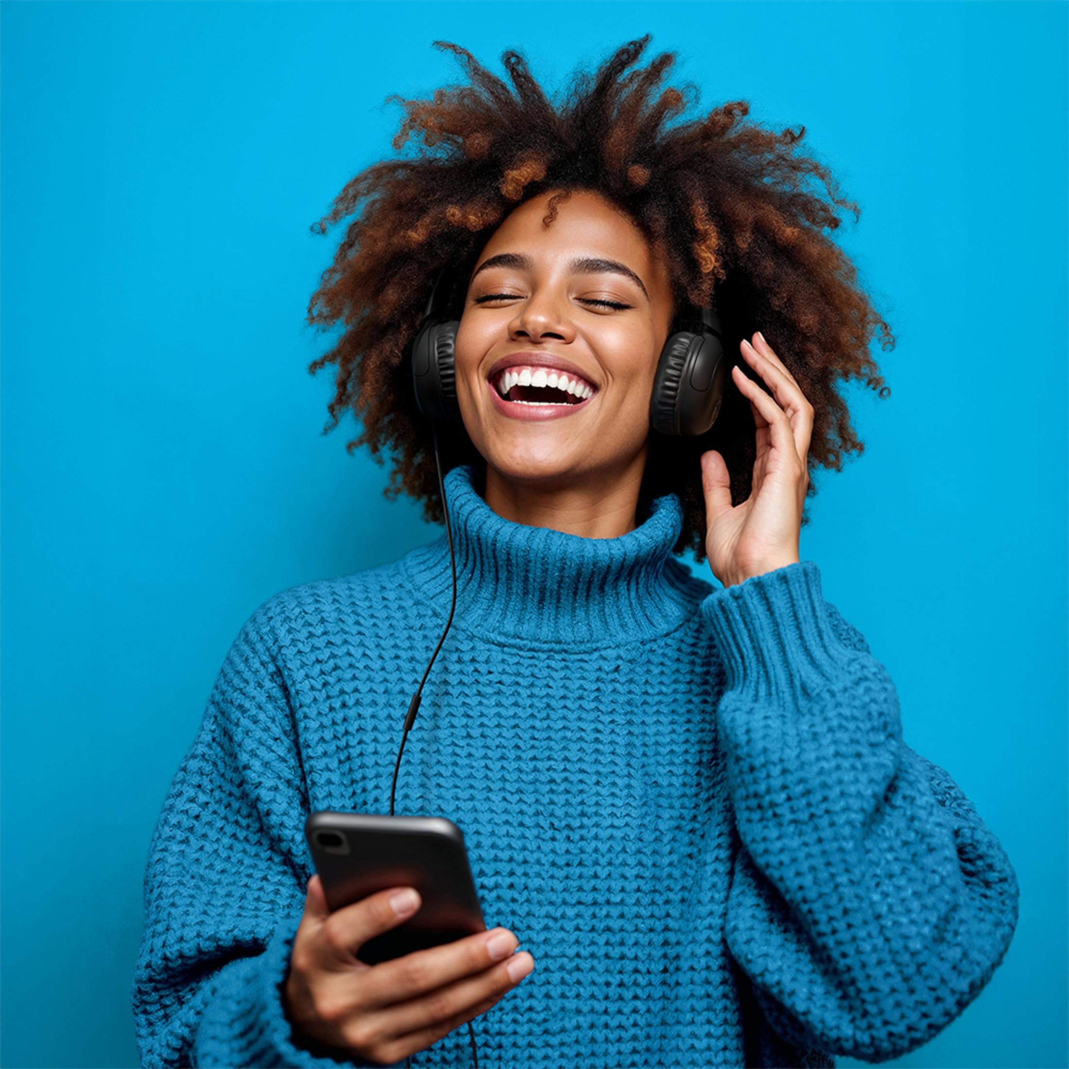 Femme avec casque et téléphone riant sur fond bleu.