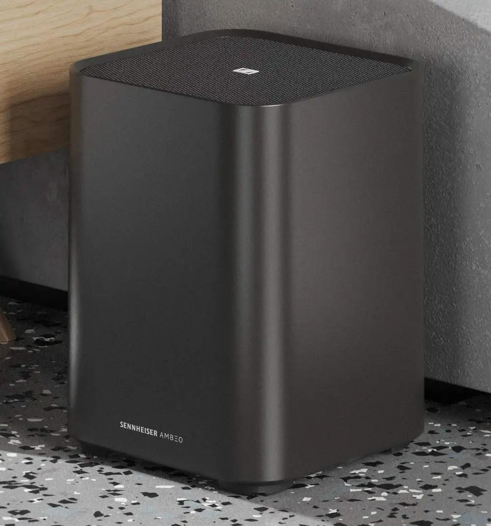 Subwoofer Sennheiser AMBEO nero con top in rete, accanto a un mobile in legno.